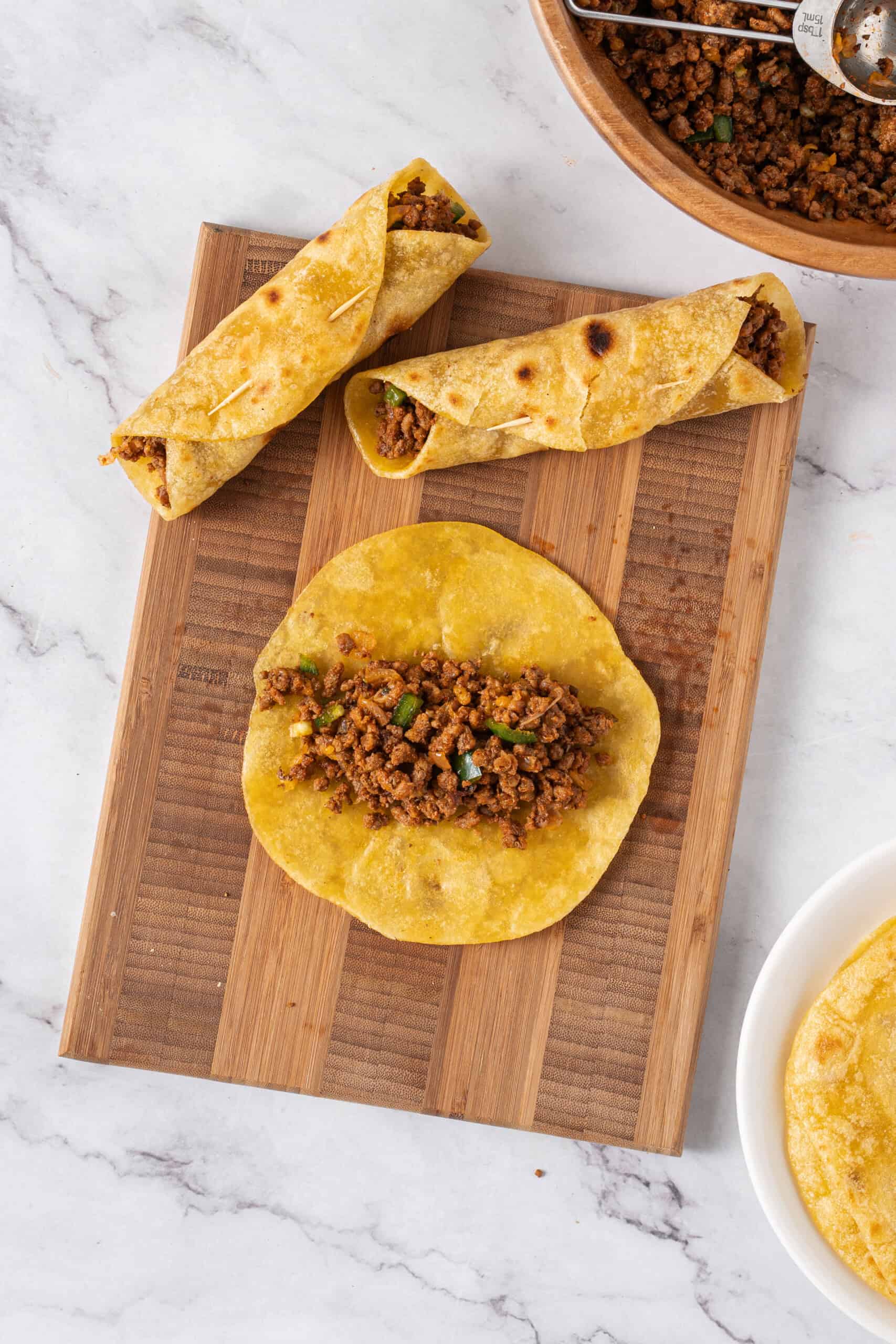 Ground beef filling spooned onto a corn tortilla for rolling into a taquito.