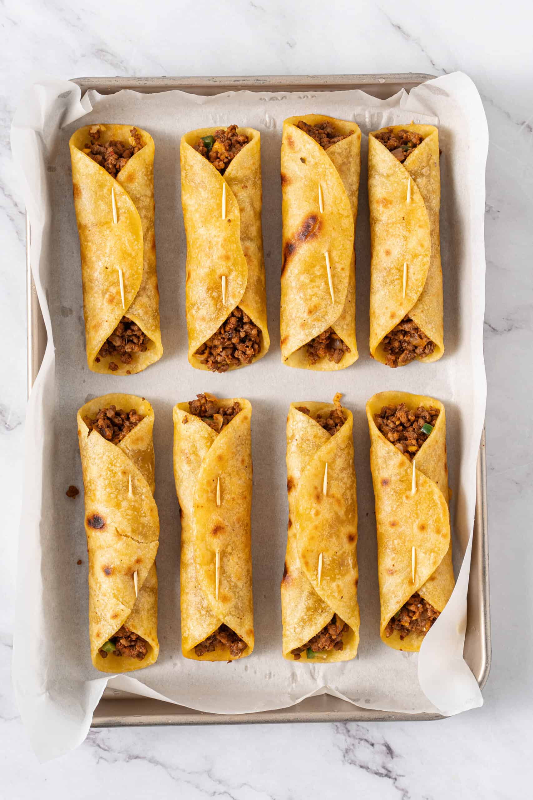 Rolled taquitos secured with toothpicks on a parchment-lined baking sheet.