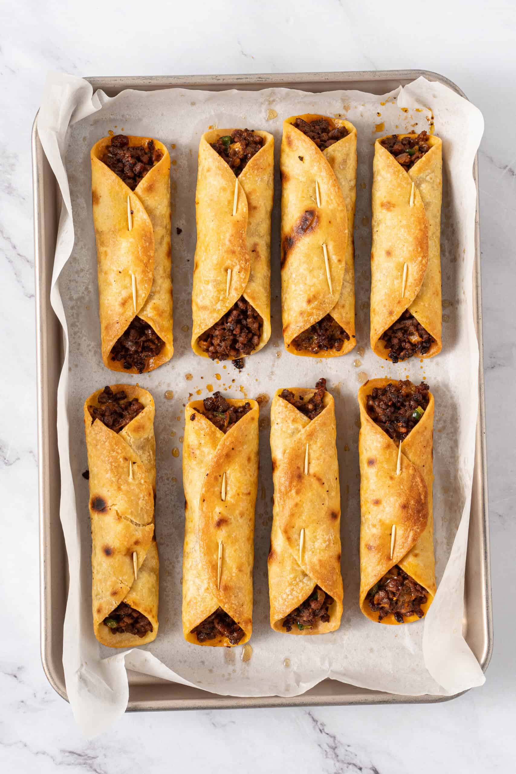 Baked taquitos with crispy golden corn tortillas on a baking sheet.