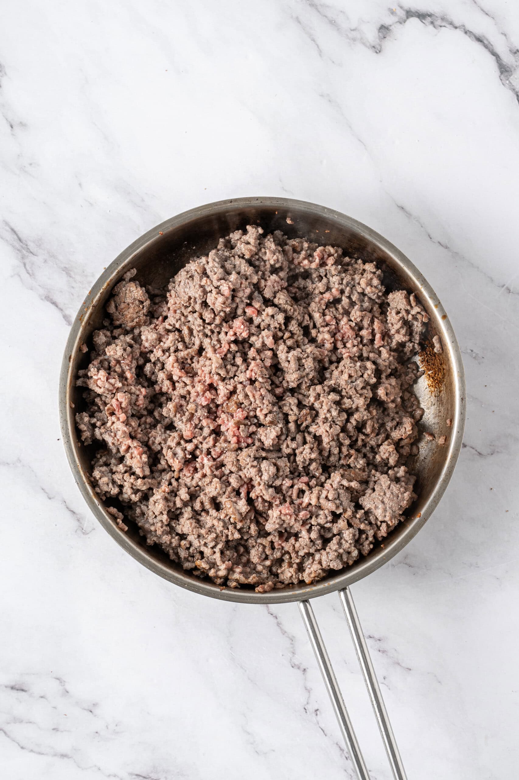 Ground beef browning in a stainless steel skillet.
