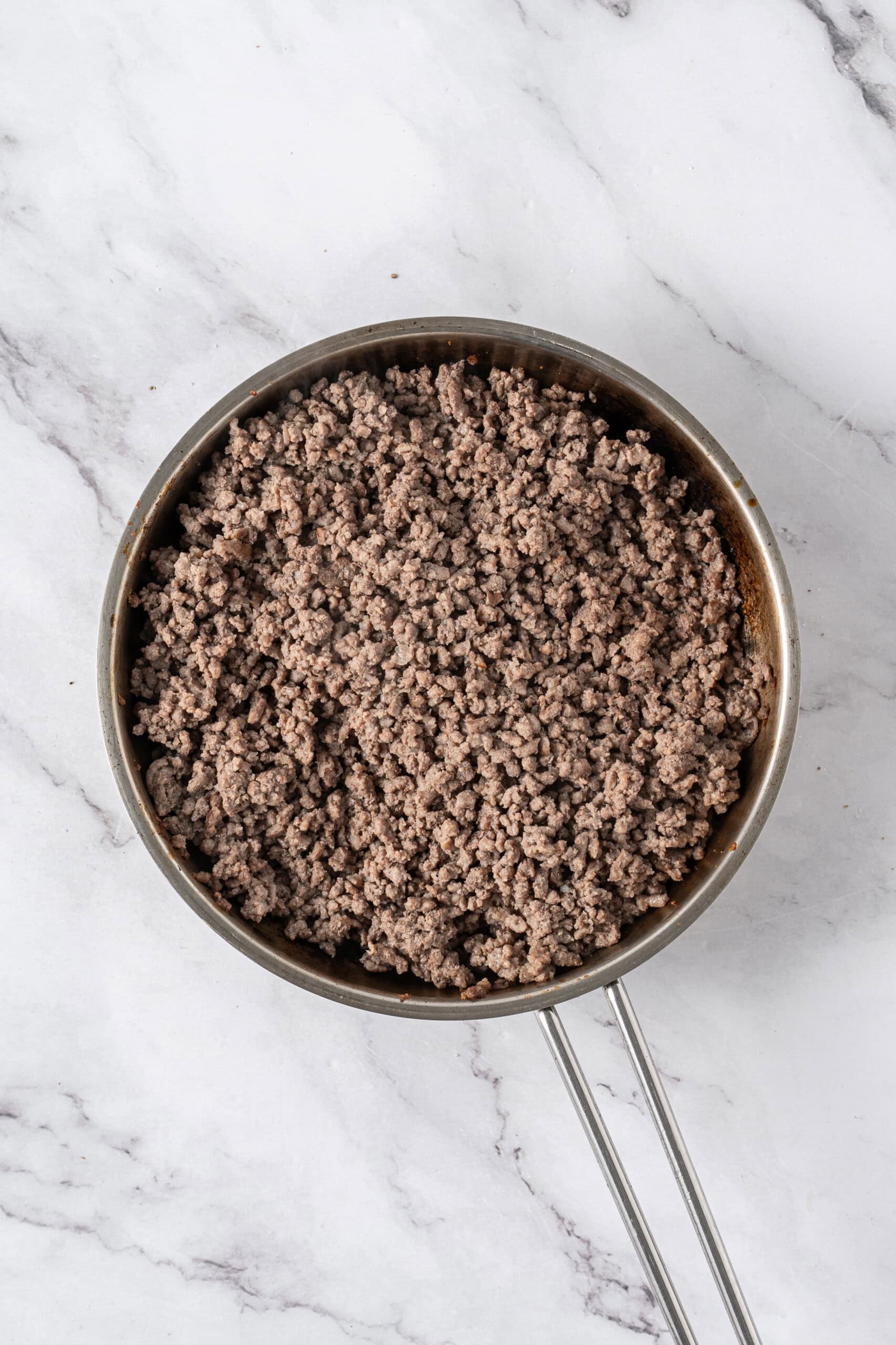 Cooked ground beef crumbled in a stainless steel skillet.