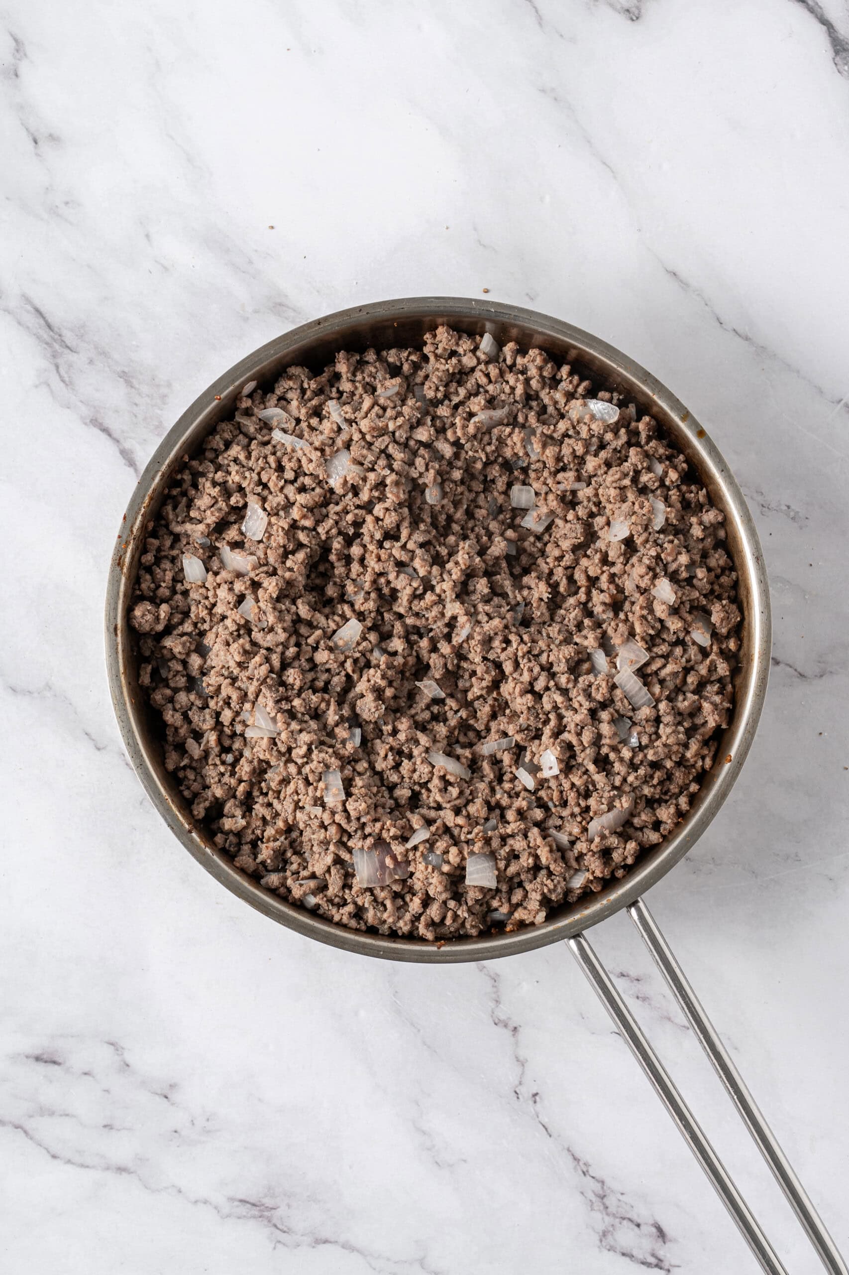 Cooked ground beef with diced onions in a stainless steel skillet.