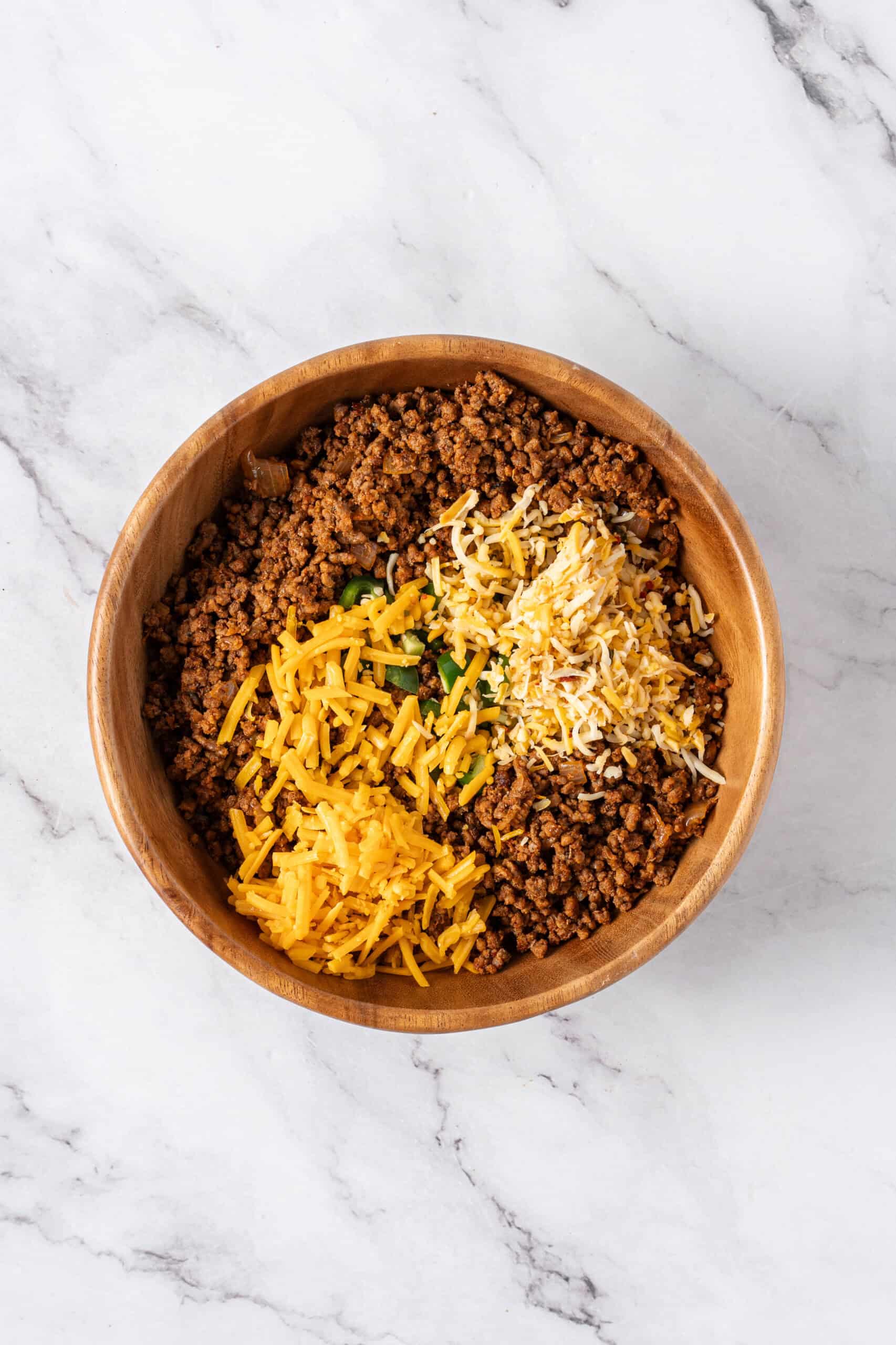 Seasoned ground beef with shredded cheese and diced jalapeños in a mixing bowl.