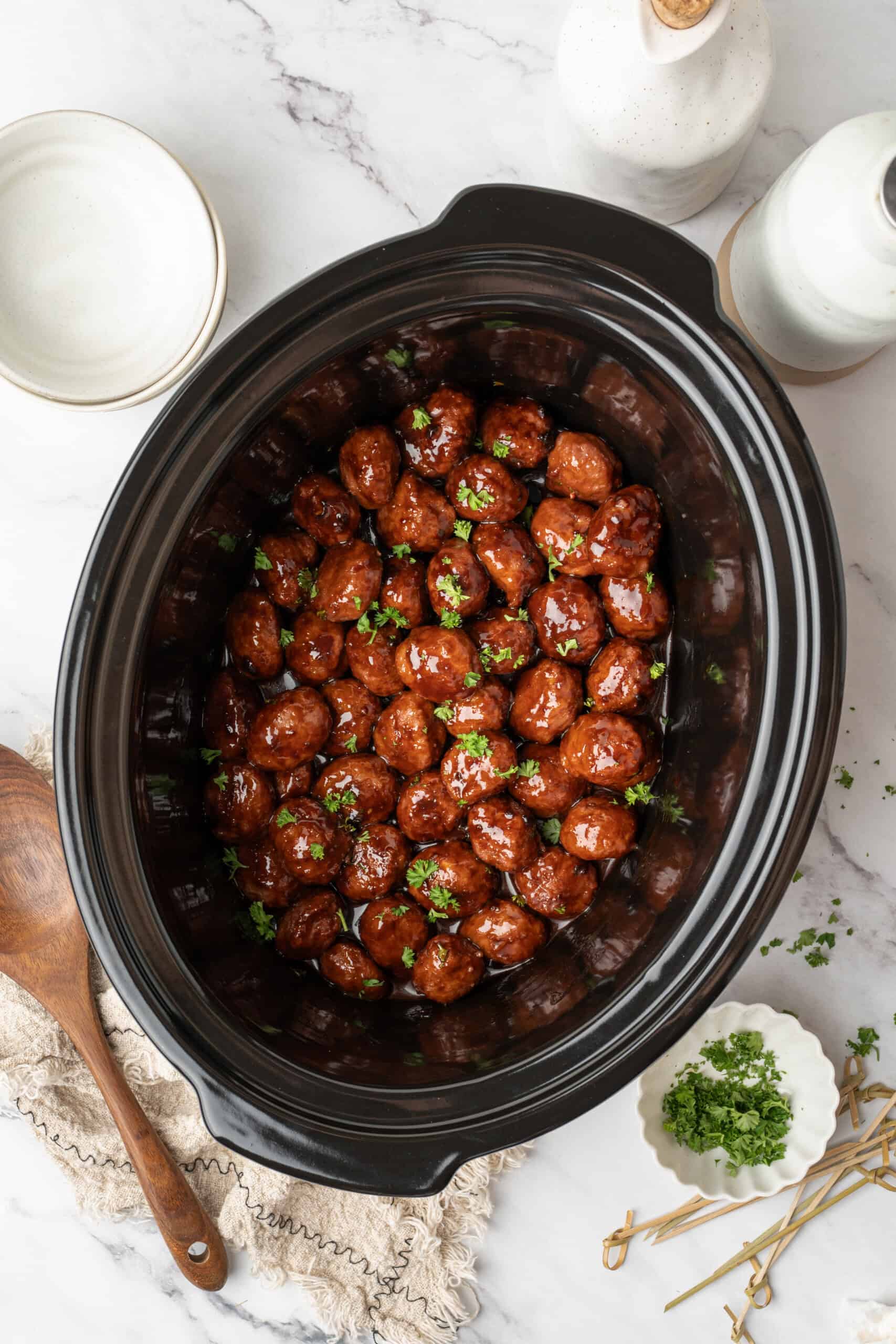 meatballs coated in a glossy sauce and garnished with fresh parsley in a slow cooker.