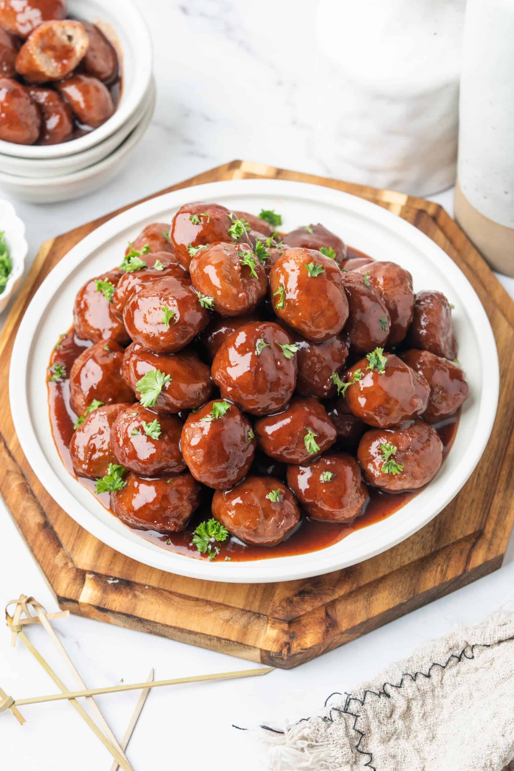 Grape jelly meatballs coated in glossy sauce and garnished with fresh parsley on a white serving platter.