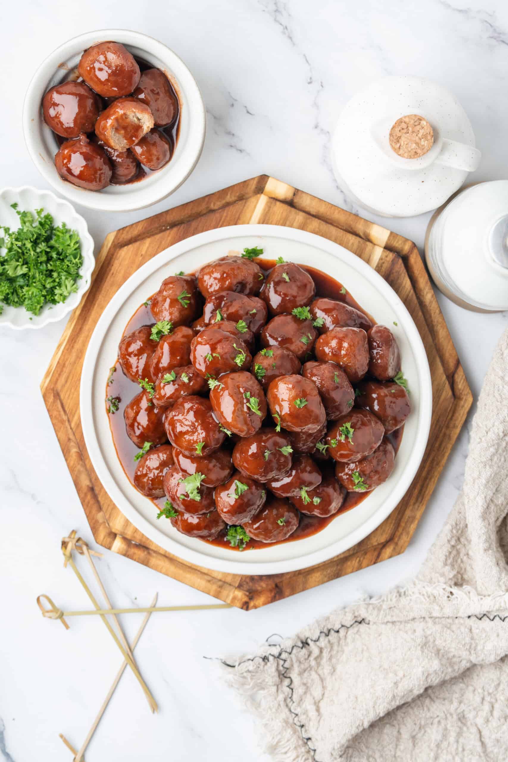 Grape jelly meatballs coated in glossy sauce and garnished with fresh parsley on a serving platter.