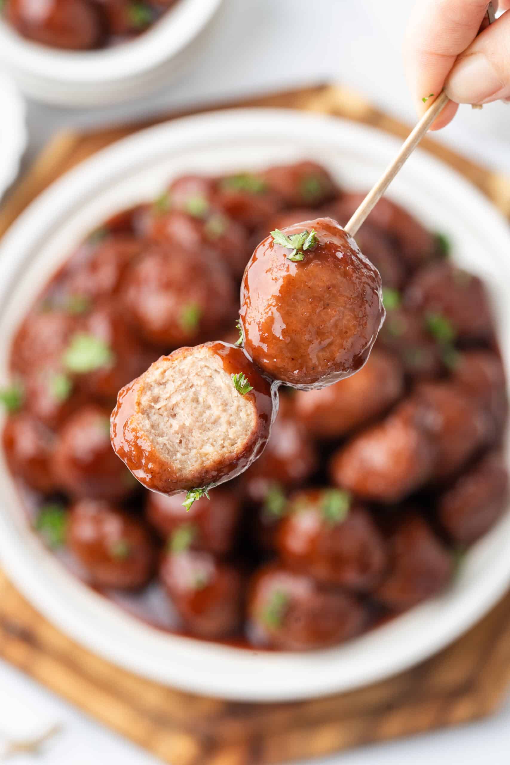 Grape jelly meatballs on skewers, coated in glossy sauce and garnished with fresh parsley.