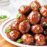 Grape jelly meatballs coated in glossy sauce and garnished with fresh parsley on a white platter.