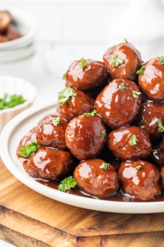 Grape jelly meatballs coated in glossy sauce and garnished with fresh parsley on a white platter.