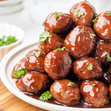 Grape jelly meatballs coated in glossy sauce and garnished with fresh parsley on a white platter.