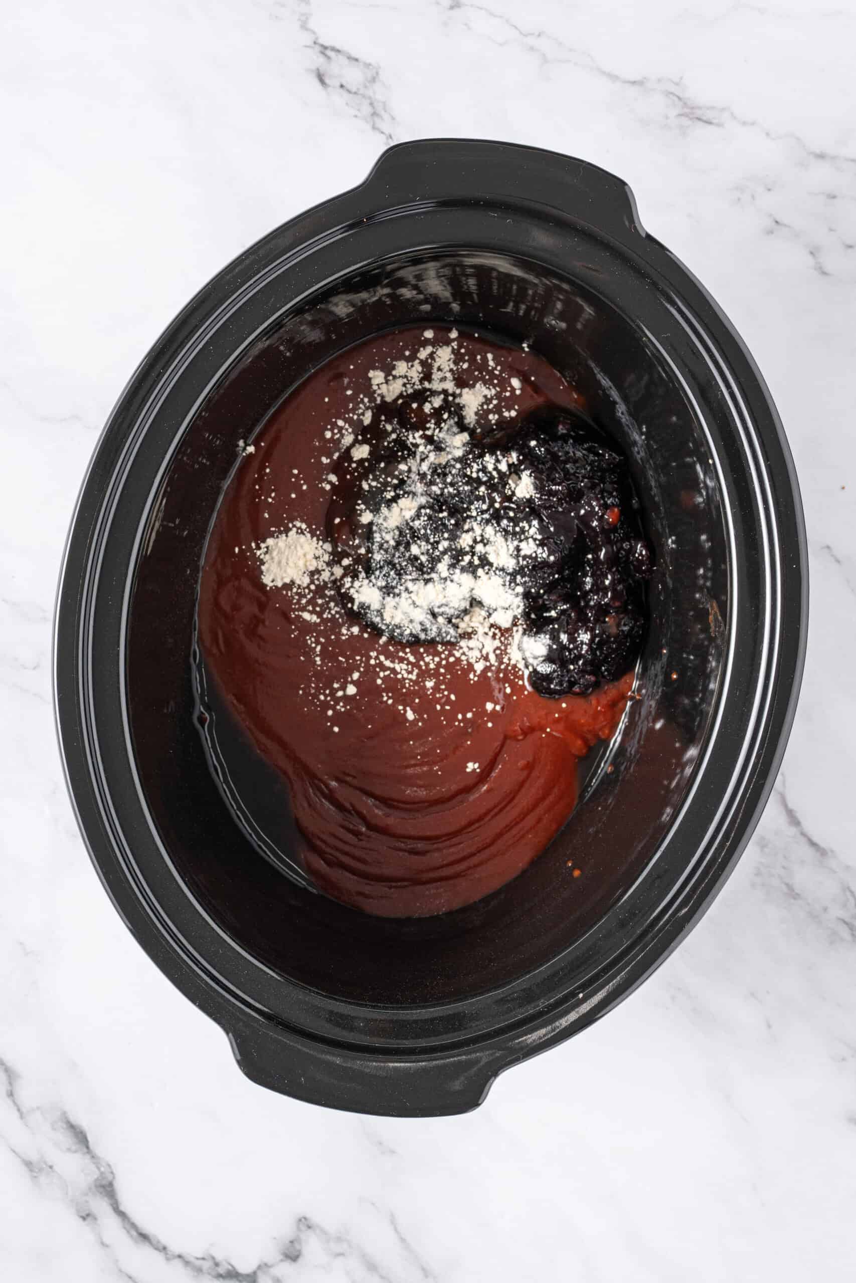Chili sauce, grape jelly, and seasonings added to a slow cooker.