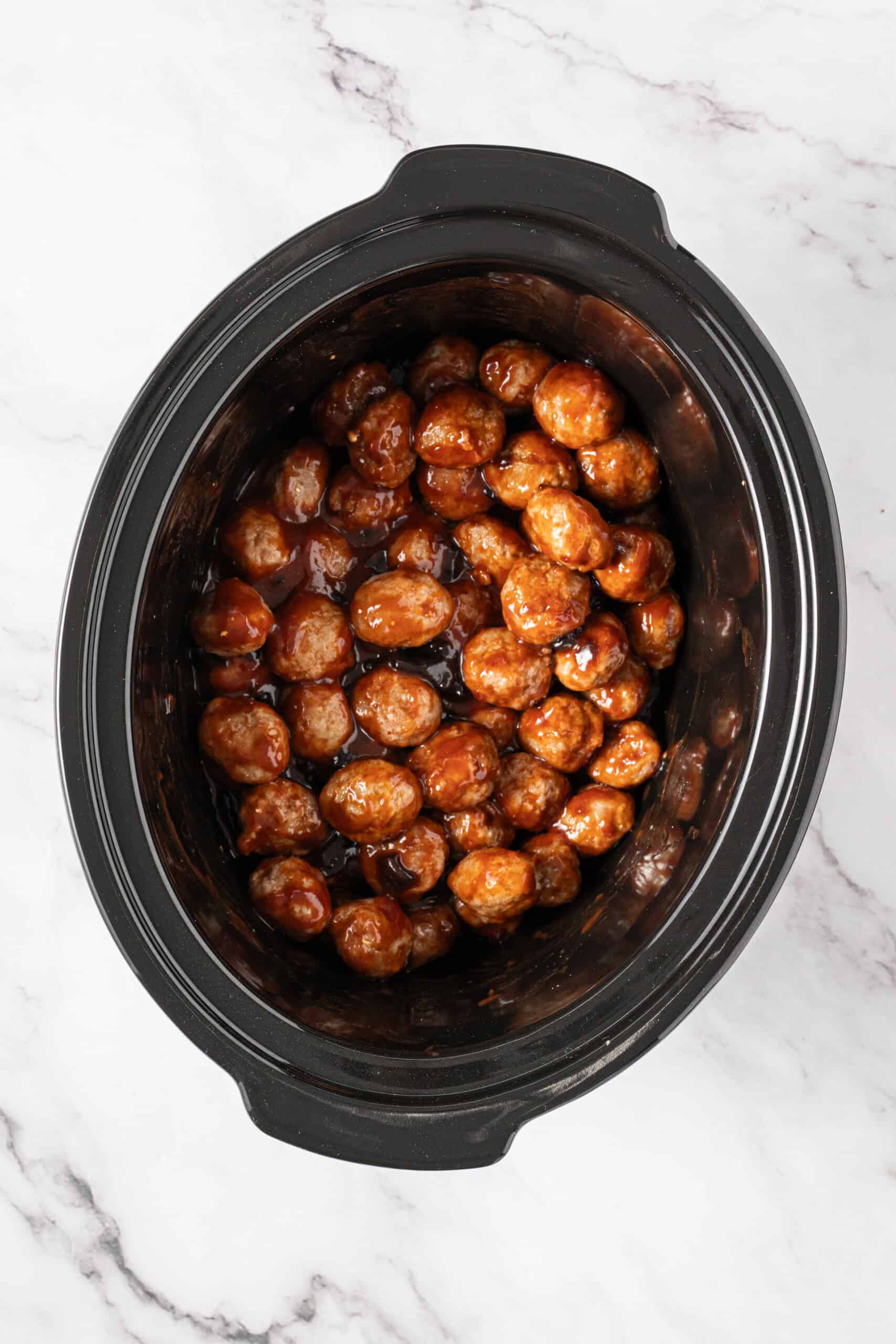 meatballs coated in a glossy chili sauce in a slow cooker.