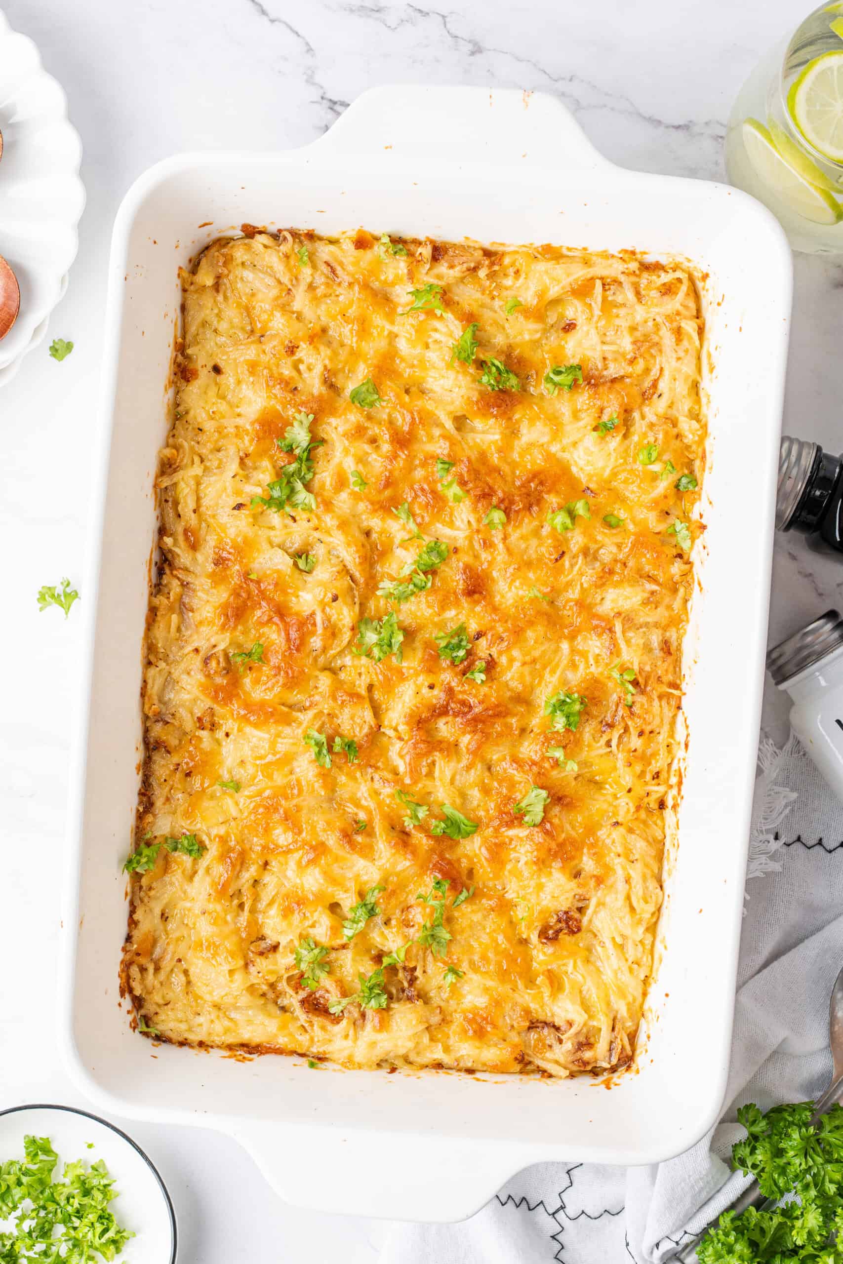 Potato casserole with golden melted cheese and fresh parsley in a white baking dish