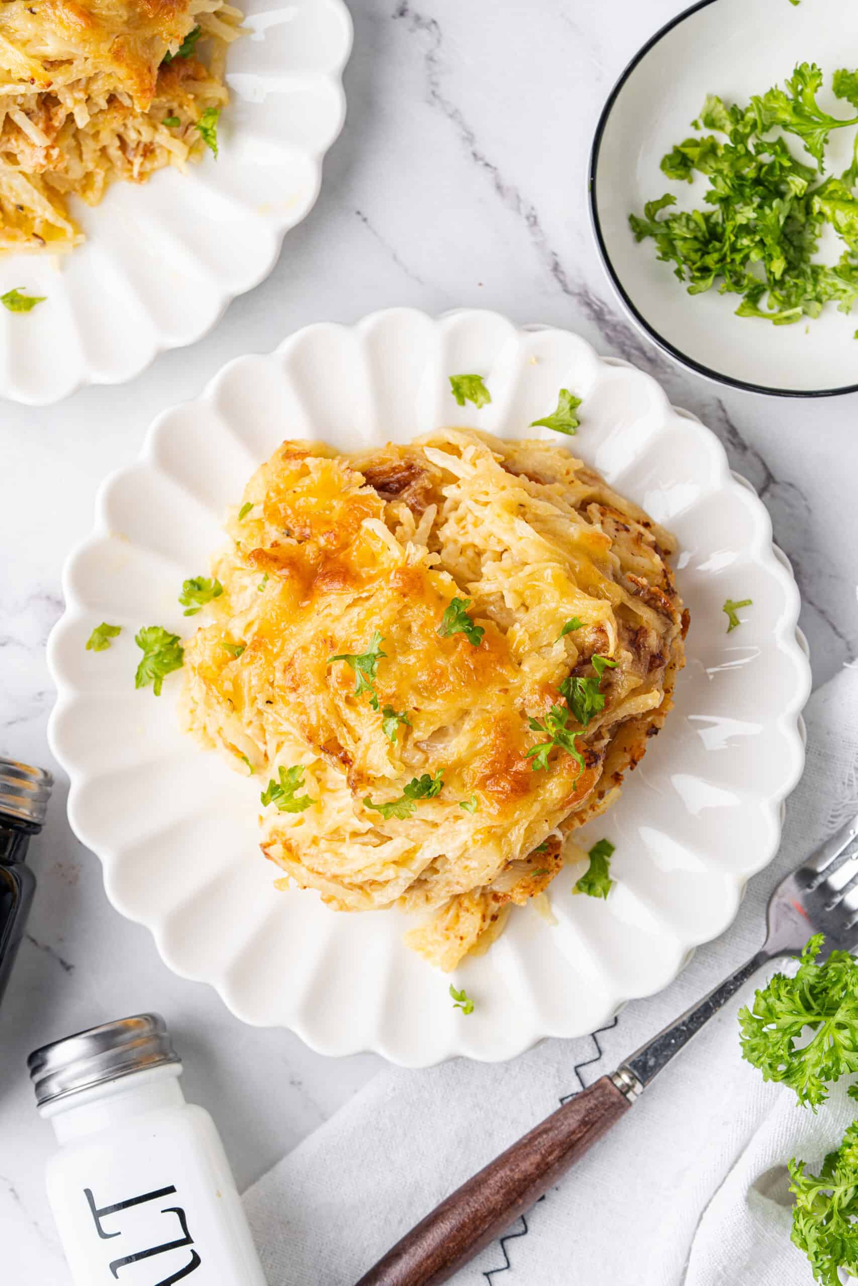 Hashbrown casserole with golden melted cheese and fresh parsley on a white plate