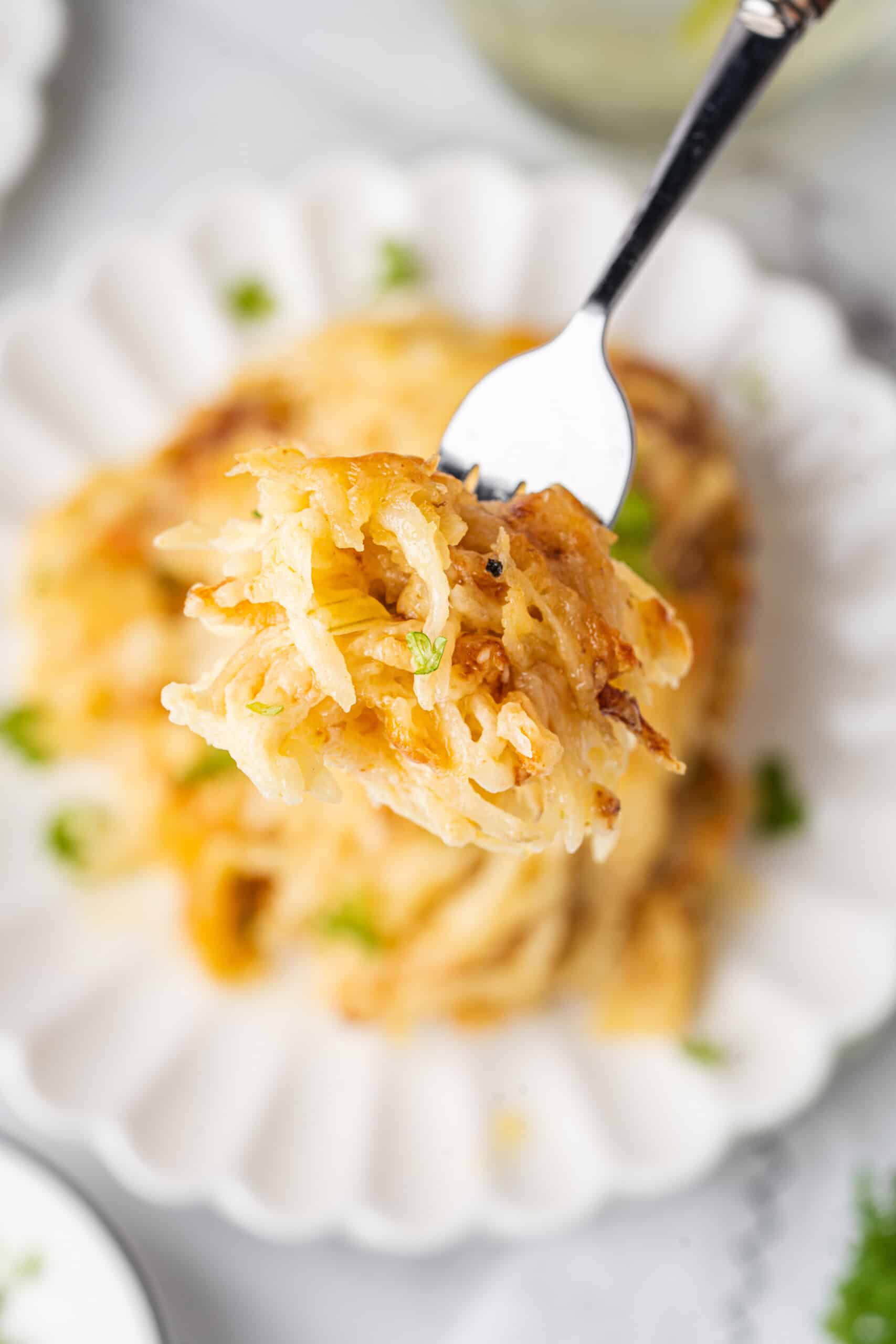 Forkful of cheesy potato casserole with fresh parsley