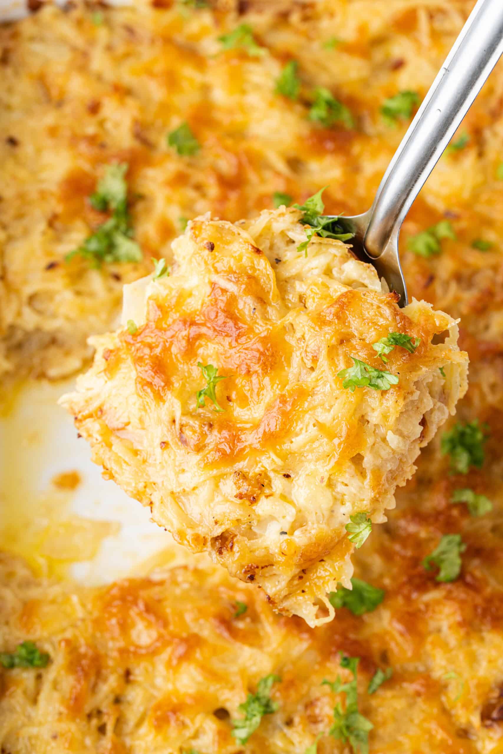 Hashbrown casserole with golden melted cheese and fresh parsley on a serving spoon