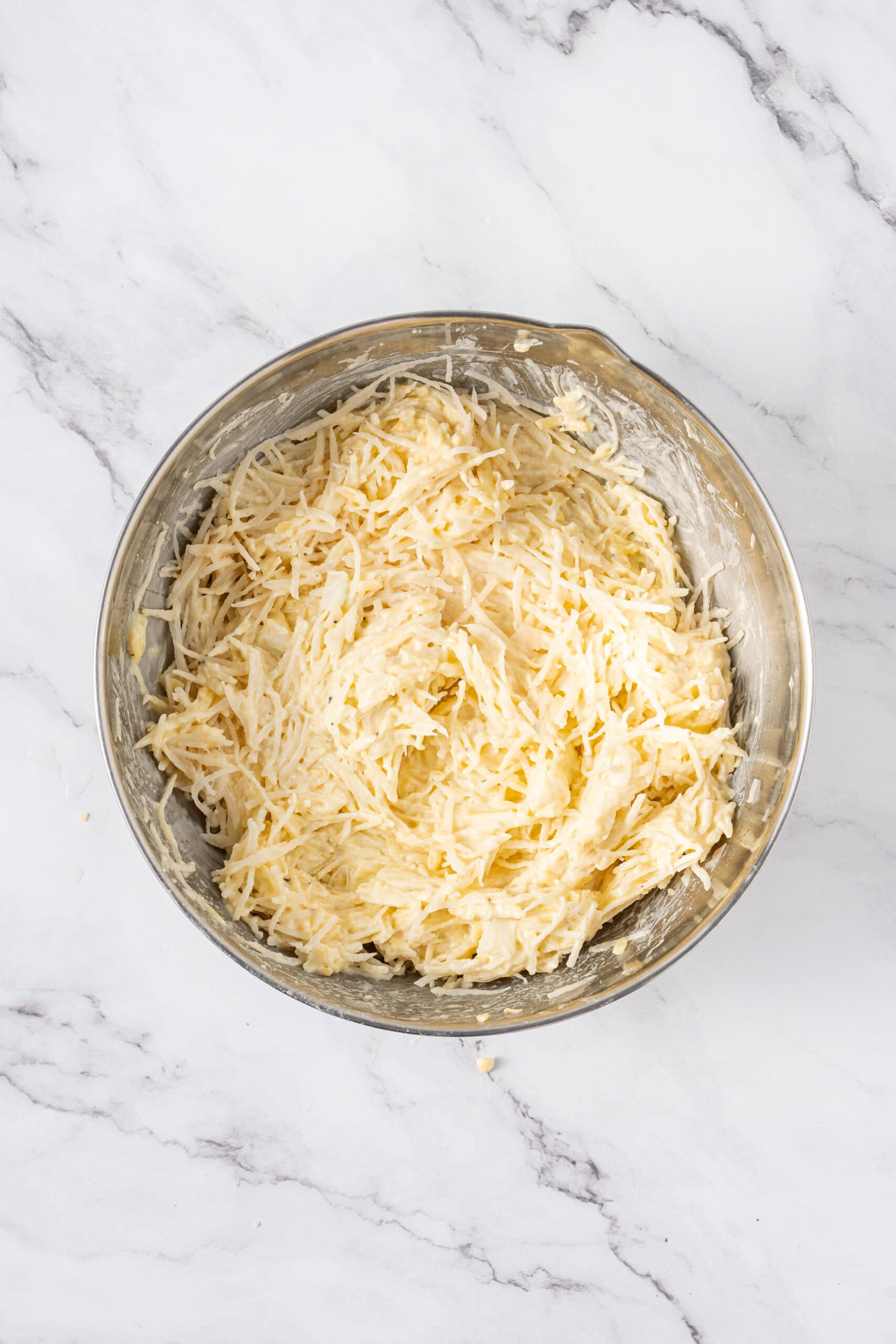 Hash browns mixed with the creamy cheese mixture in a large bowl.