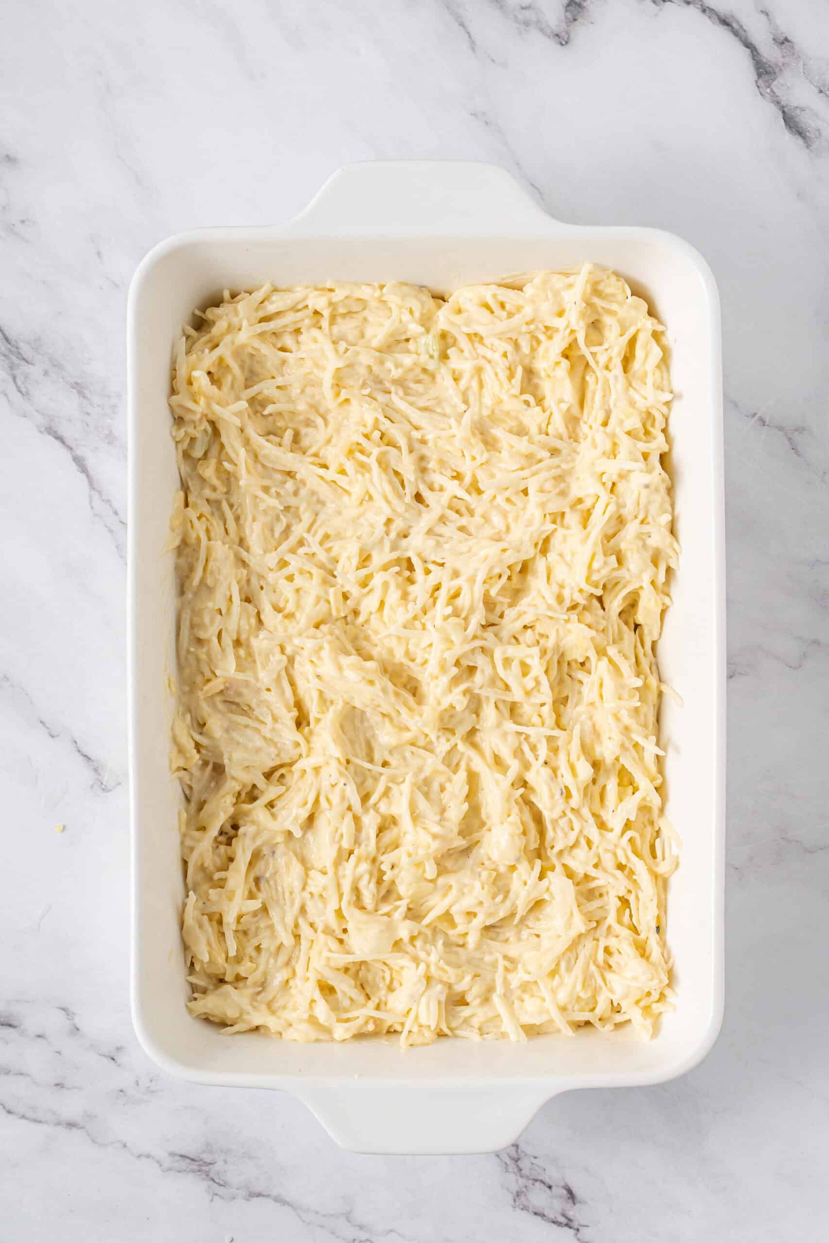 Hashbrown mixture spread evenly in a white baking dish.