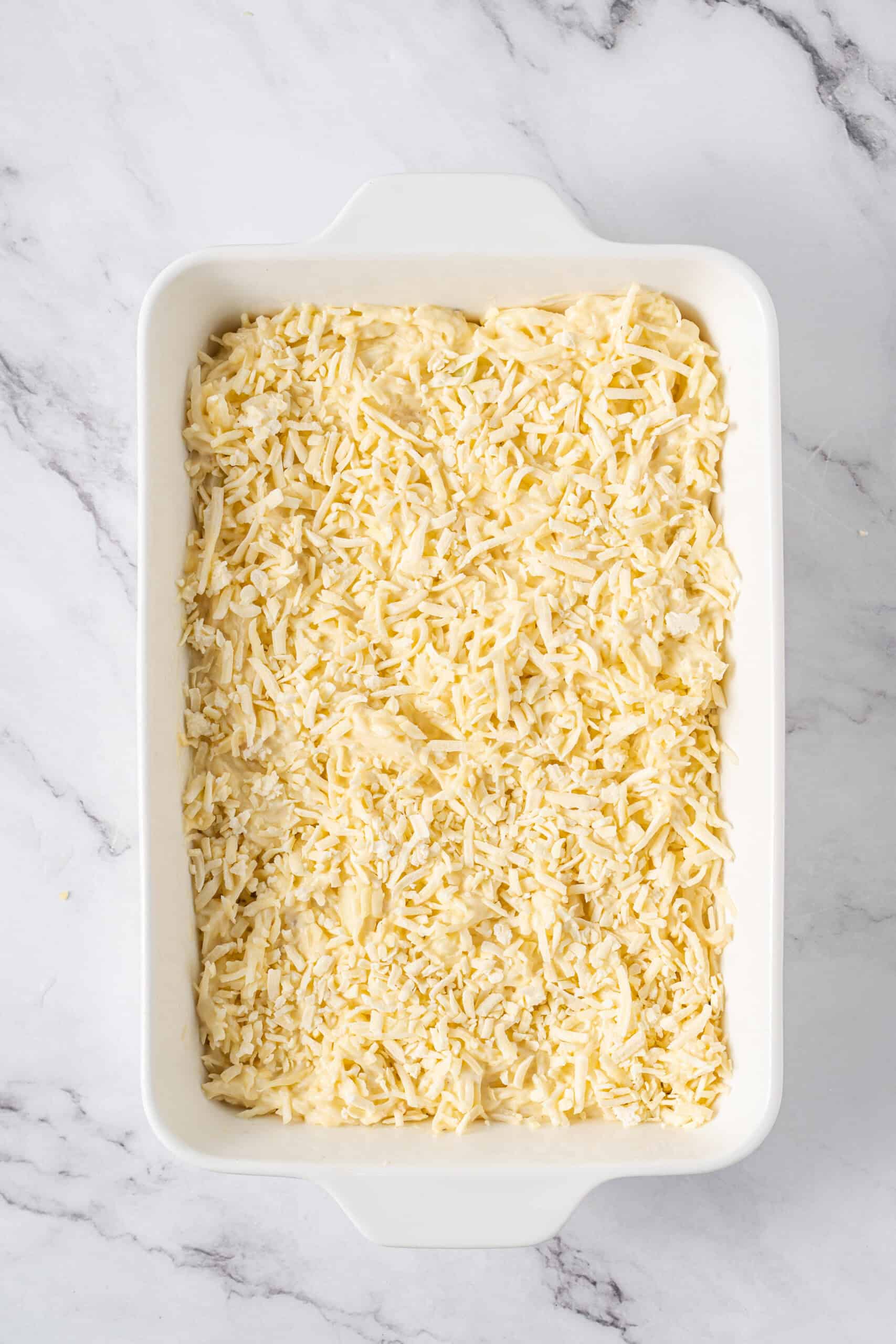 Hashbrown mixture topped with shredded cheese in a white baking dish.