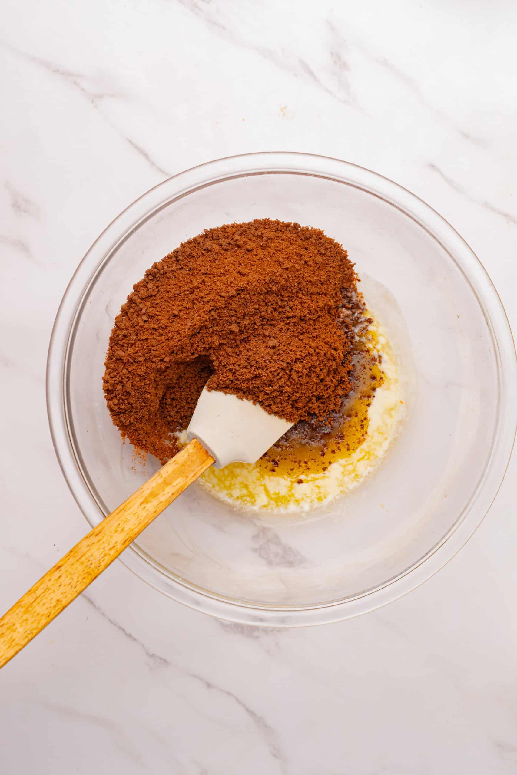Melted butter and brown cookie crumbs in a glass mixing bowl with a spatula.