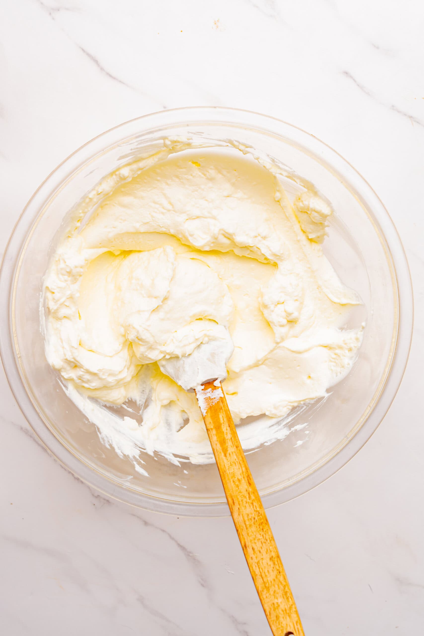 beaten cream cheese in a glass mixing bowl with a spatula.