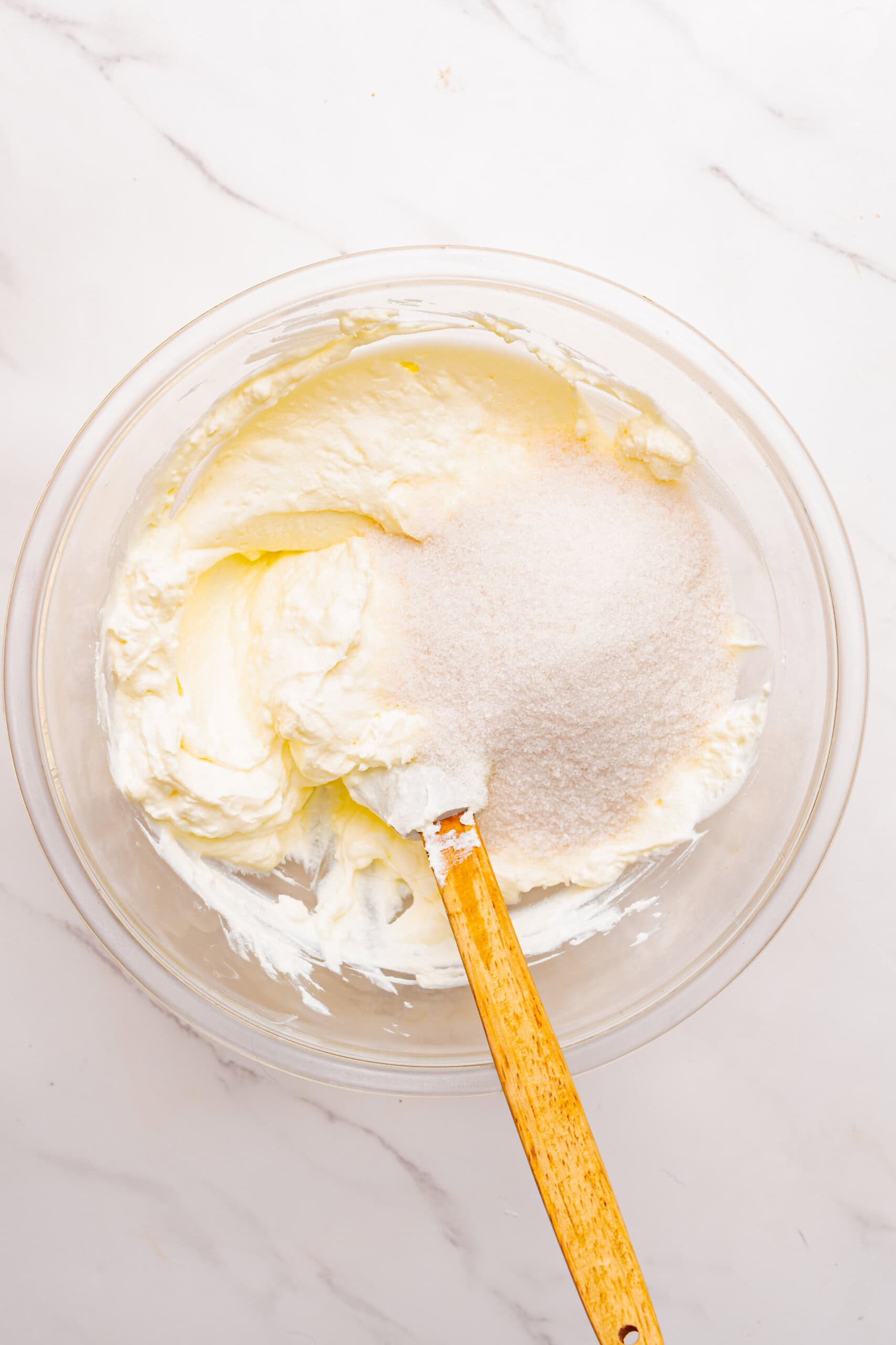 cream cheese topped with granulated sugar in a glass mixing bowl.