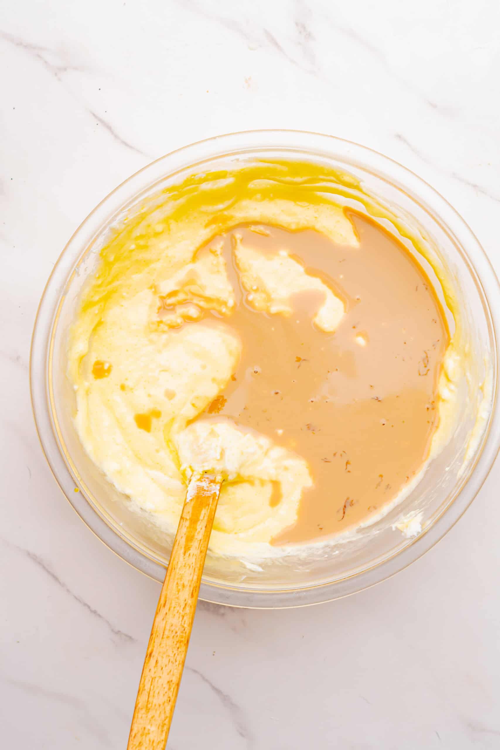 Irish cream liqueur added to the cream cheese and egg mixture in a glass bowl.