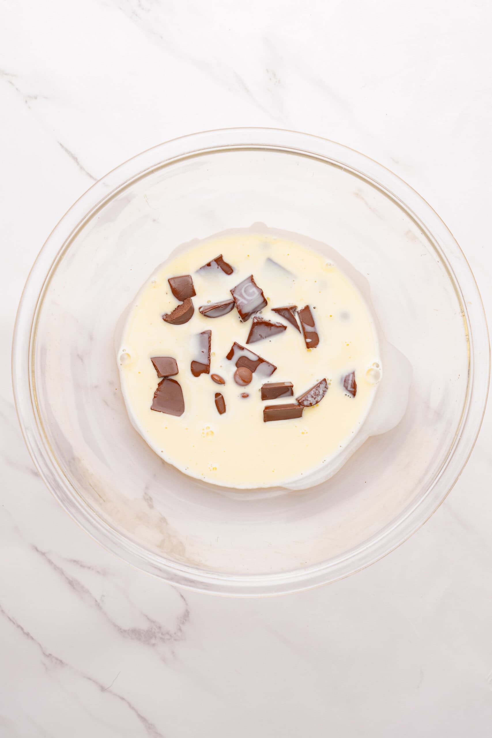 Chopped chocolate and heavy cream in a glass bowl for making ganache.