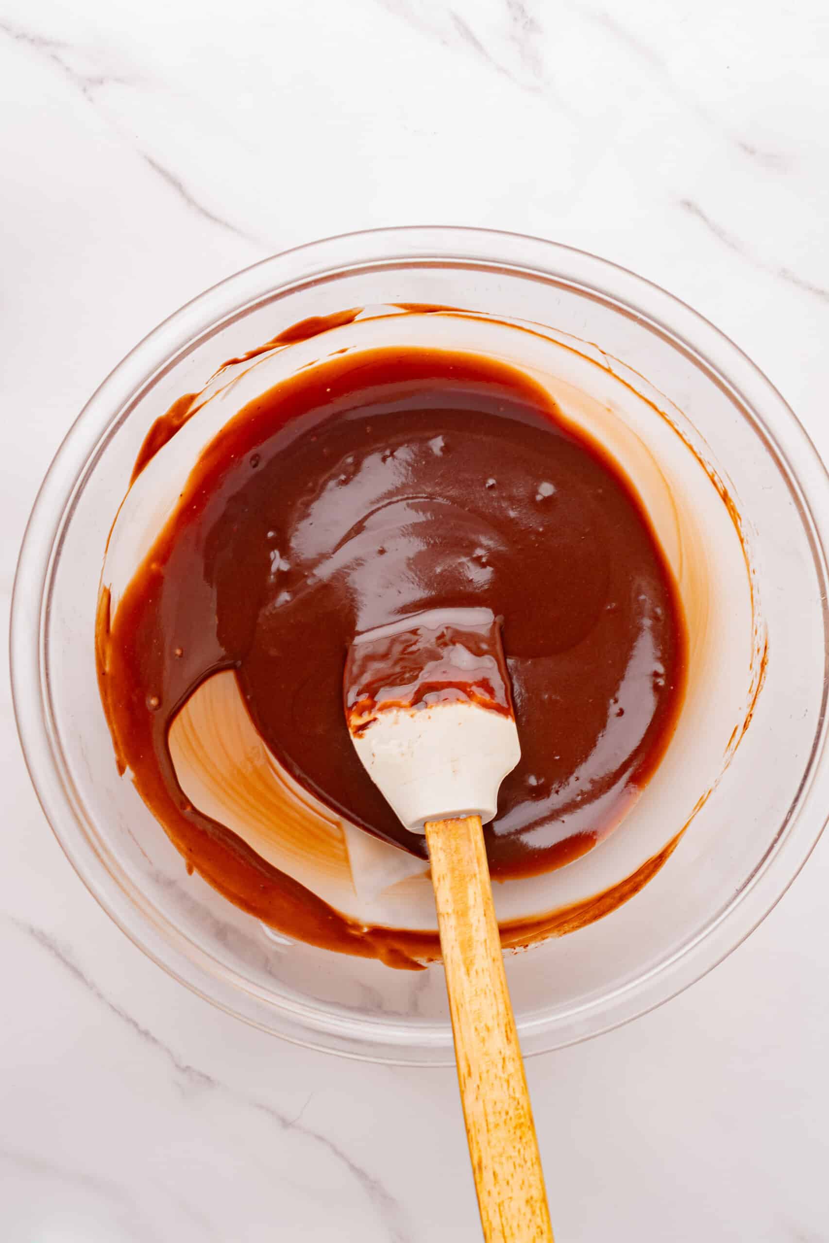Smooth chocolate ganache stirred together in a glass mixing bowl.