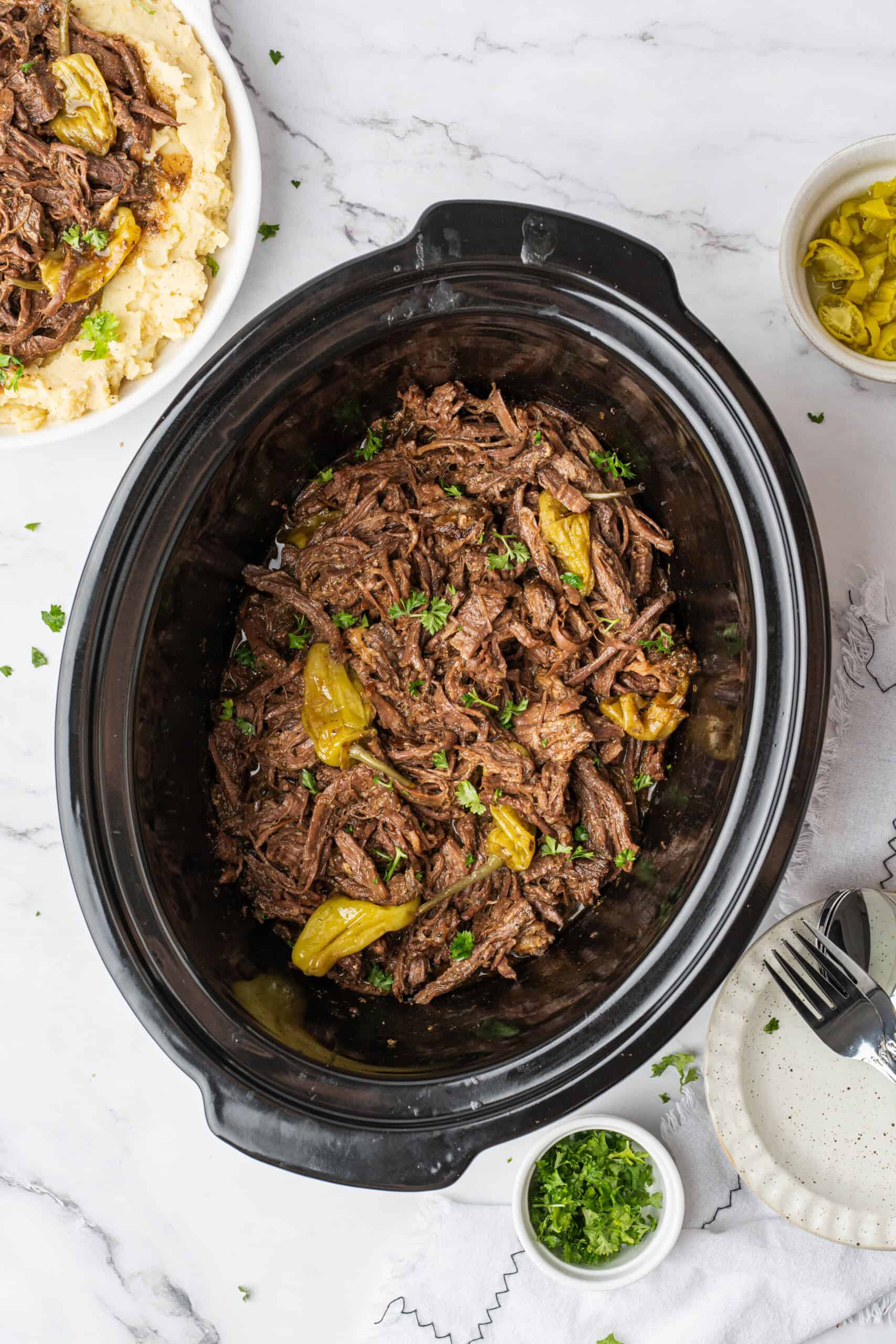 Shredded Mississippi pot roast with pepperoncini and parsley in a slow cooker.