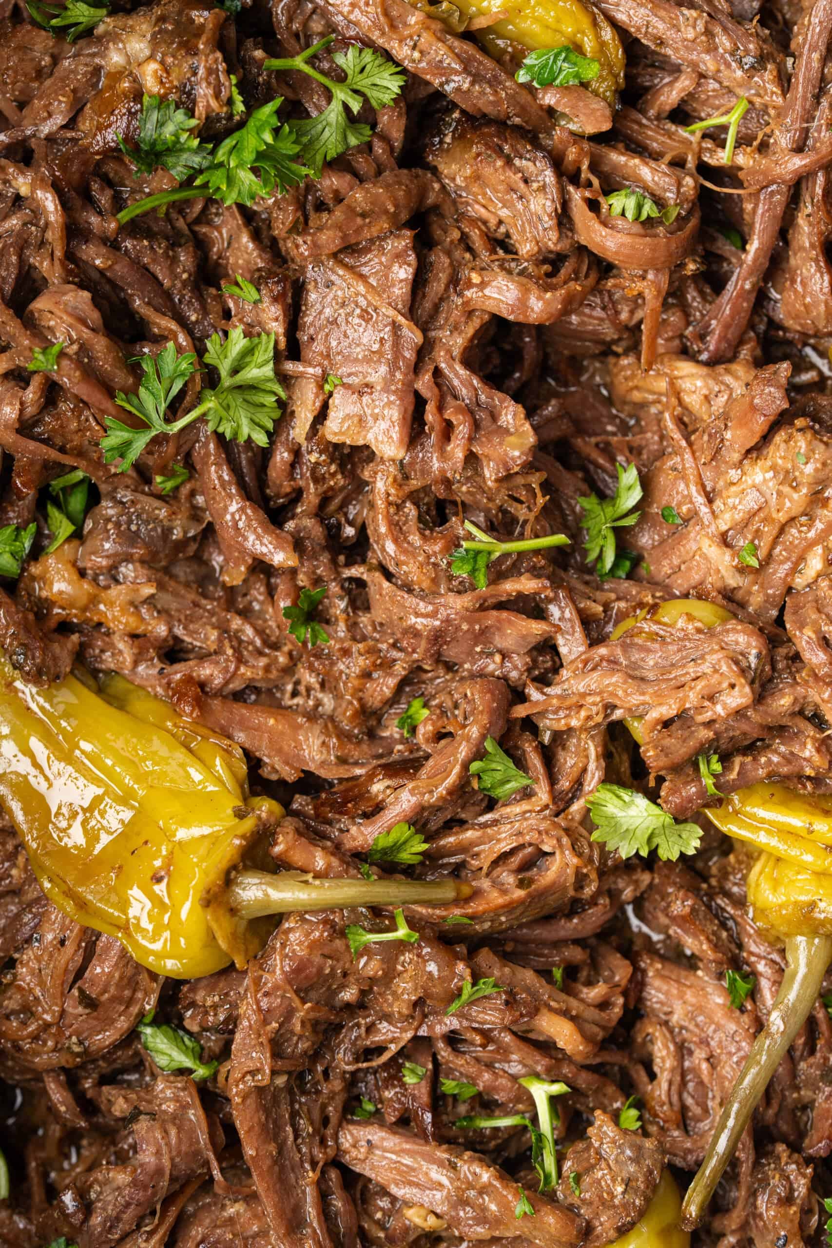 Close-up of shredded Mississippi pot roast with pepperoncini and fresh parsley.