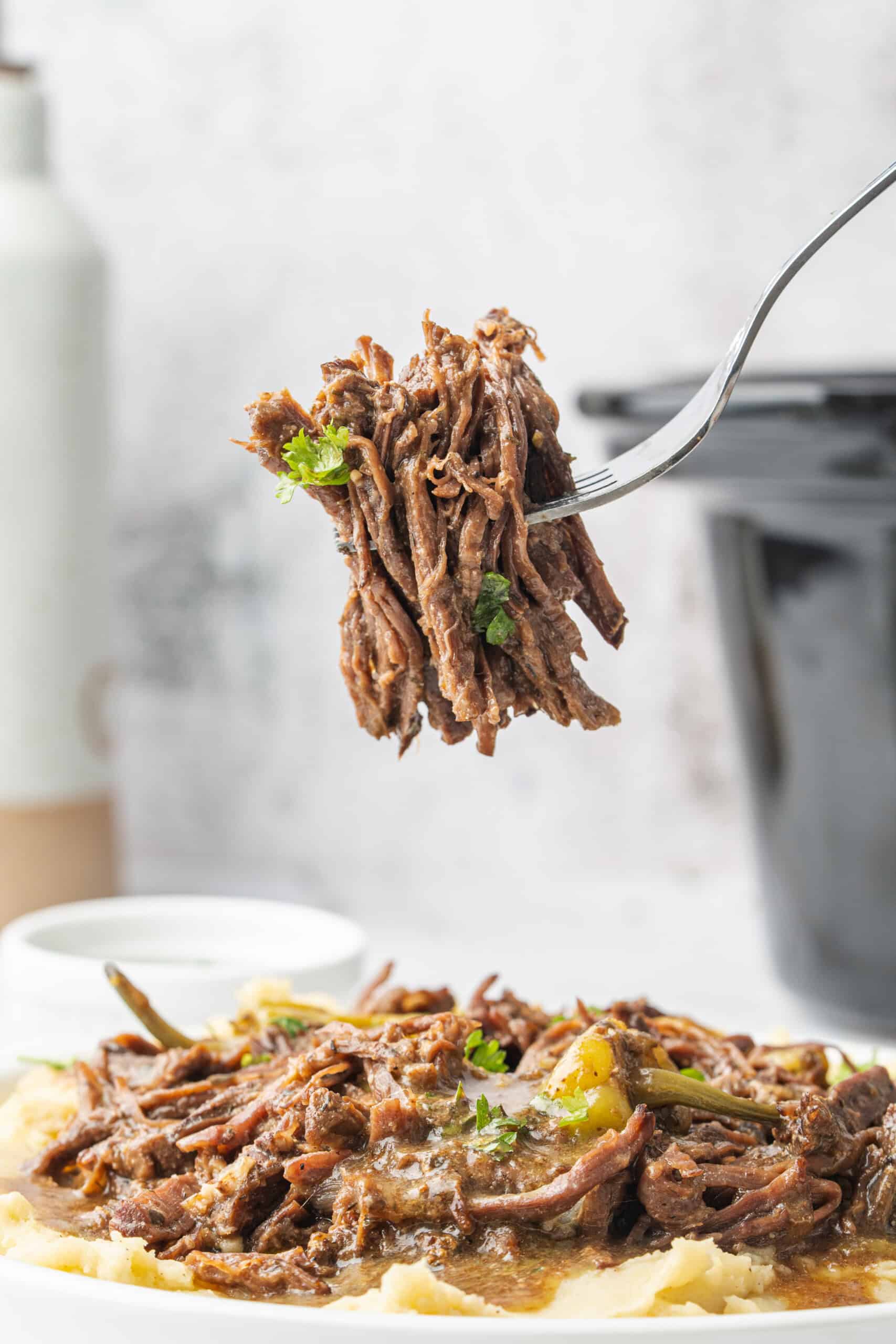 Fork holding a bite of shredded Mississippi pot roast over mashed potatoes.