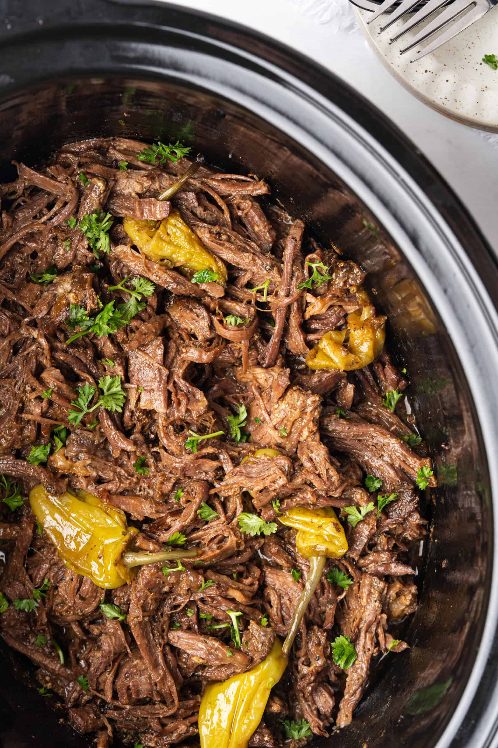 Shredded Mississippi pot roast with pepperoncini and fresh parsley in a slow cooker.