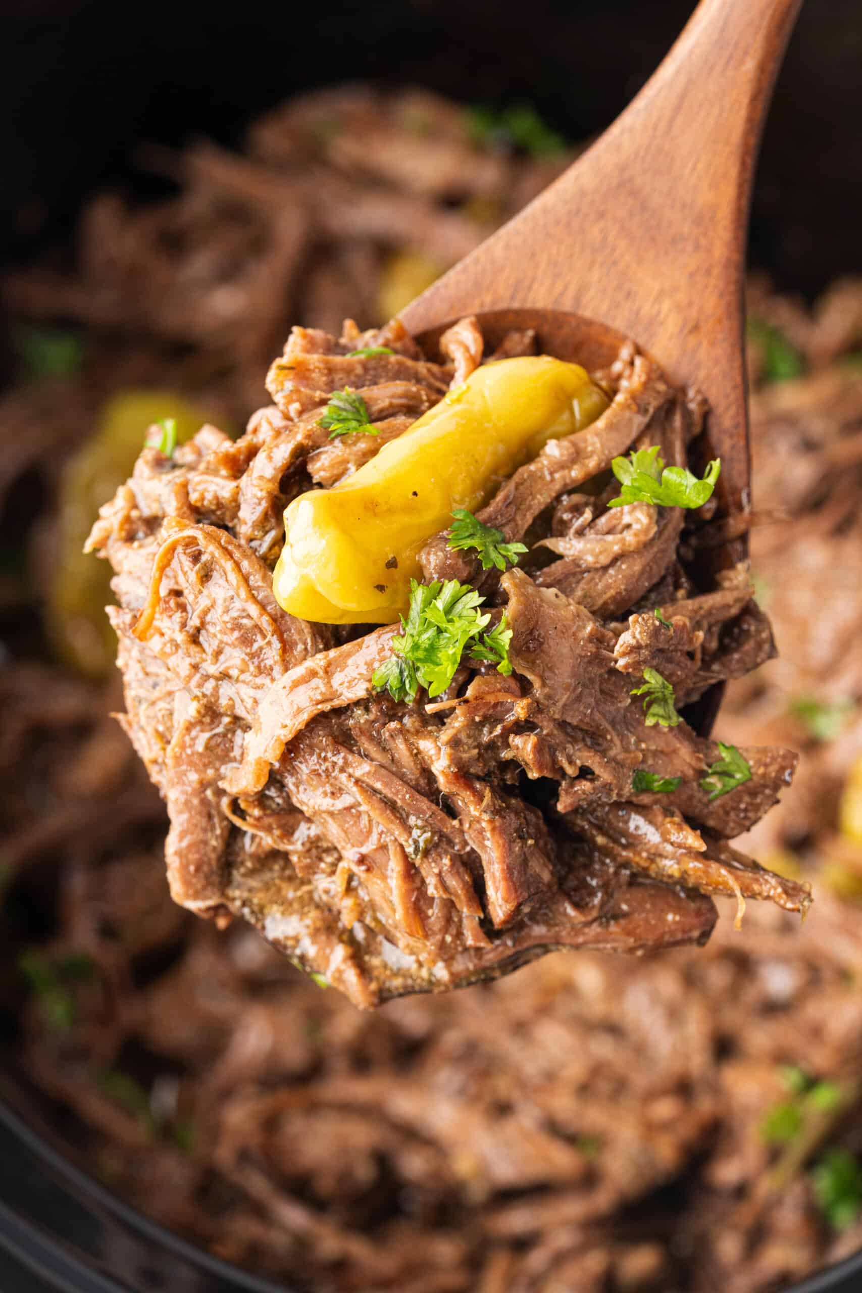 Shredded Mississippi pot roast with pepperoncini and parsley on a wooden spoon.