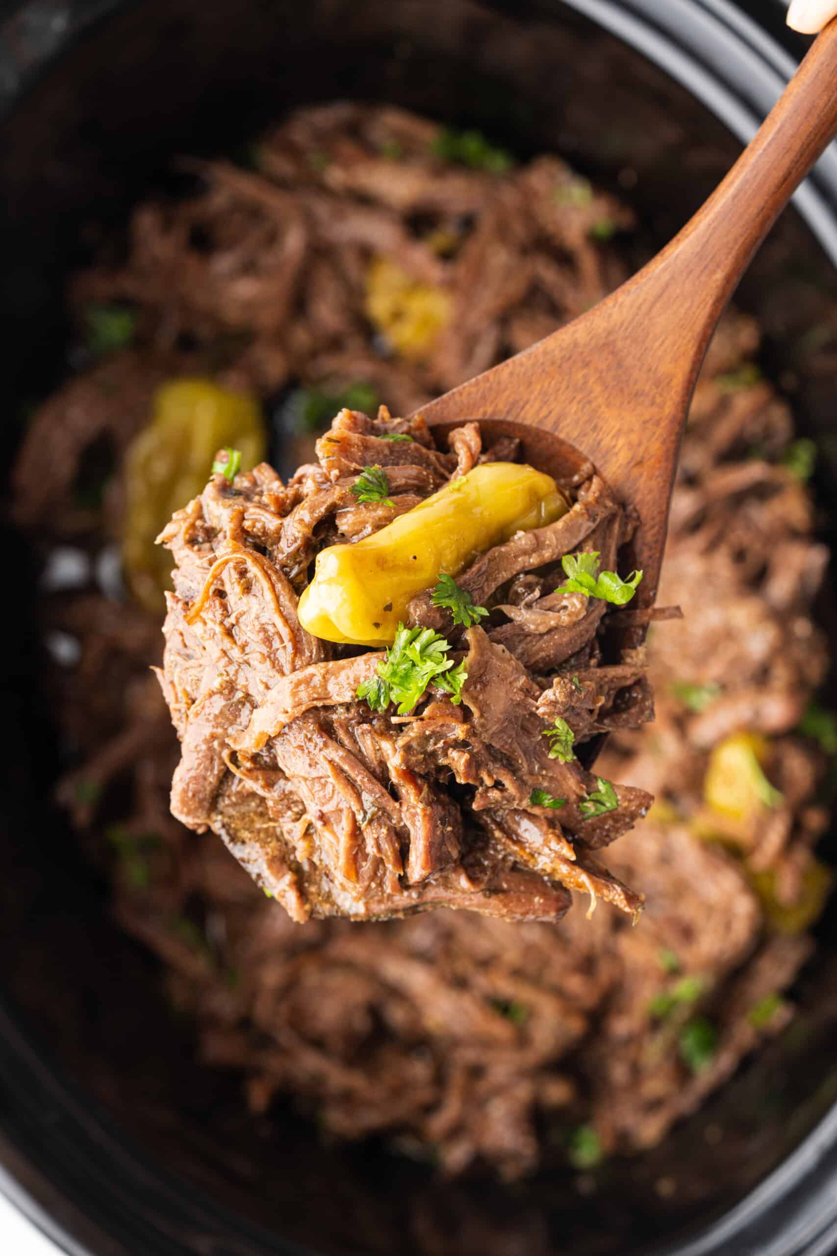 Shredded Mississippi pot roast with pepperoncini and parsley on a wooden spoon.