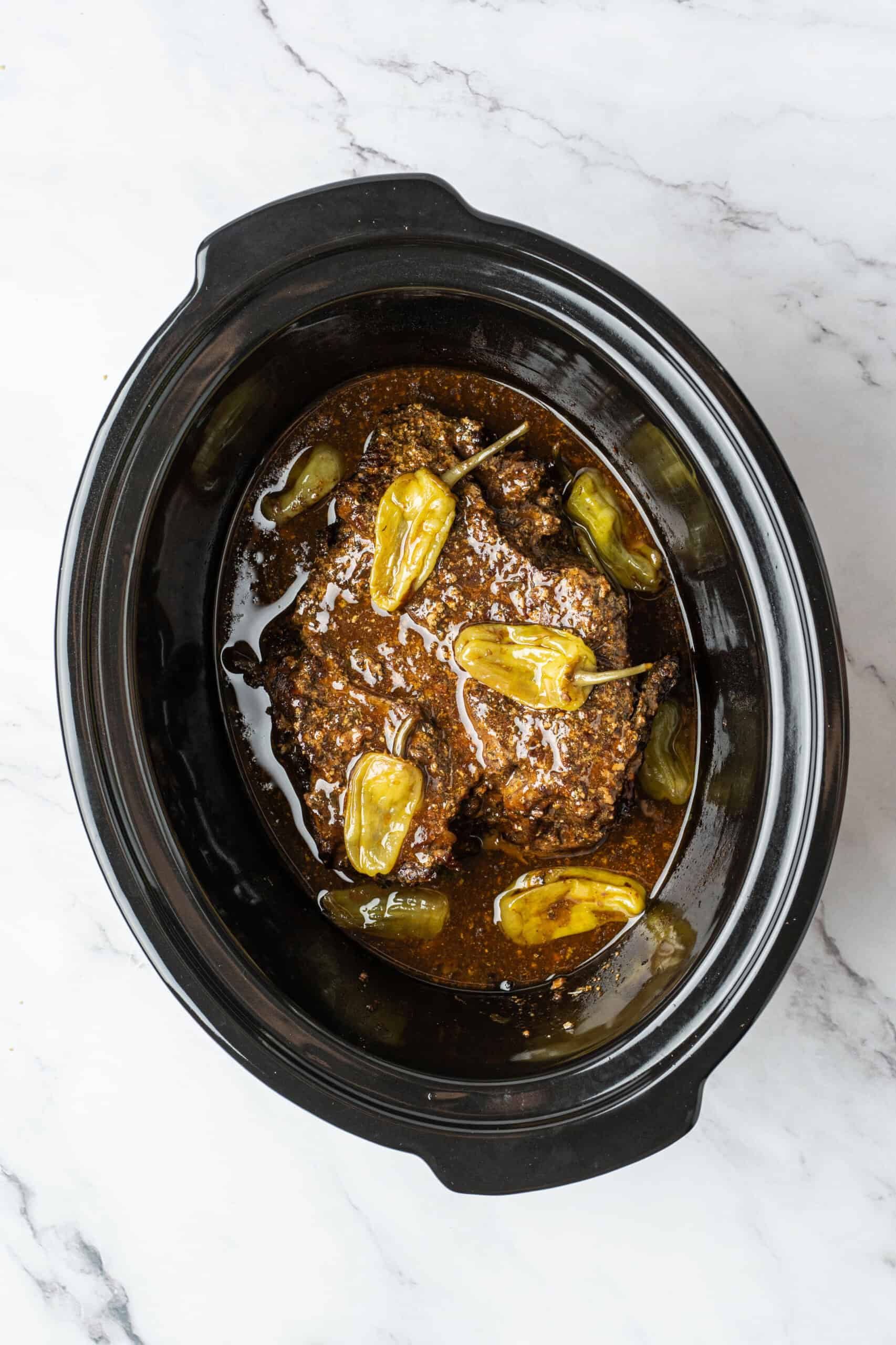 Cooked beef roast with pepperoncini and juices in a slow cooker.