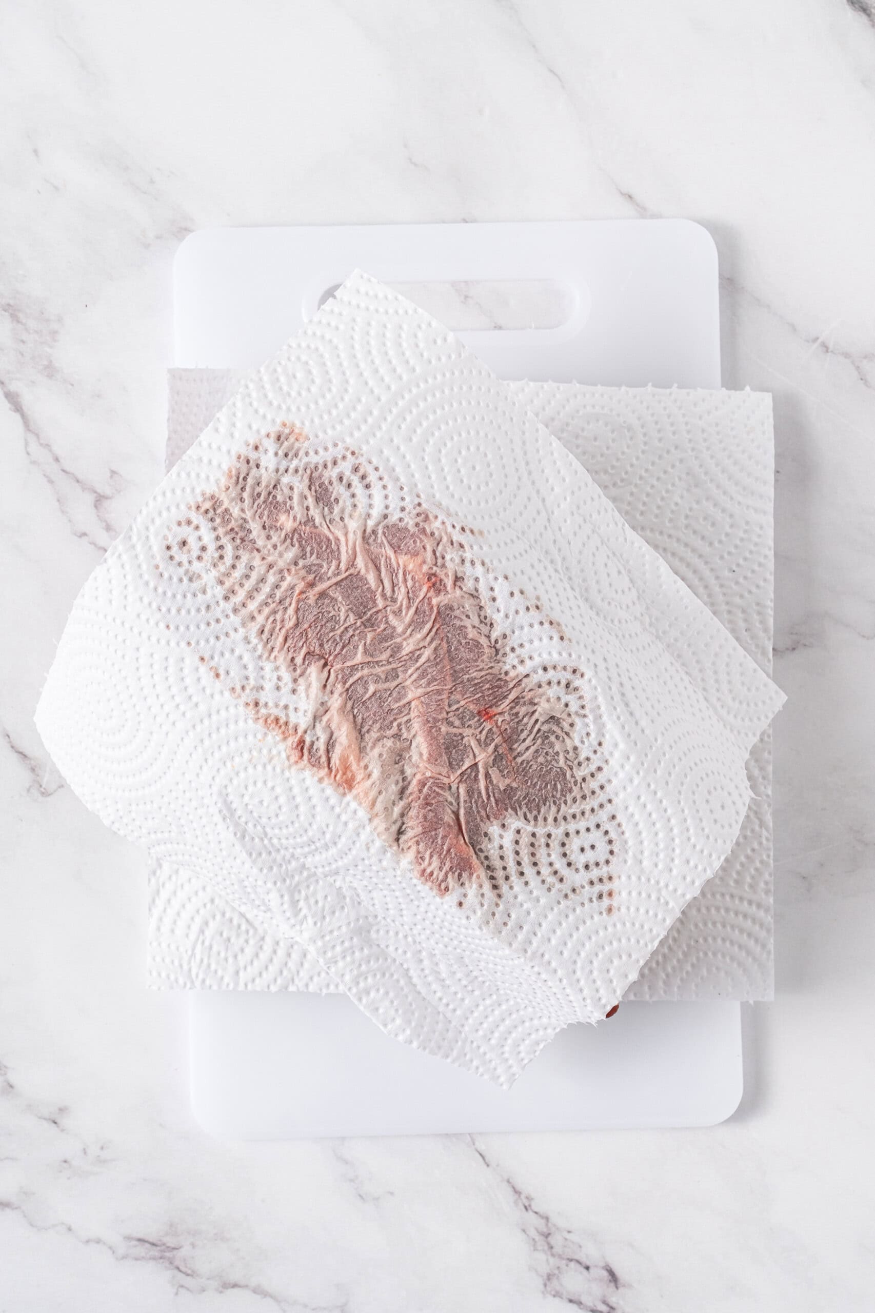 Raw beef roast patted dry with paper towels on a cutting board.