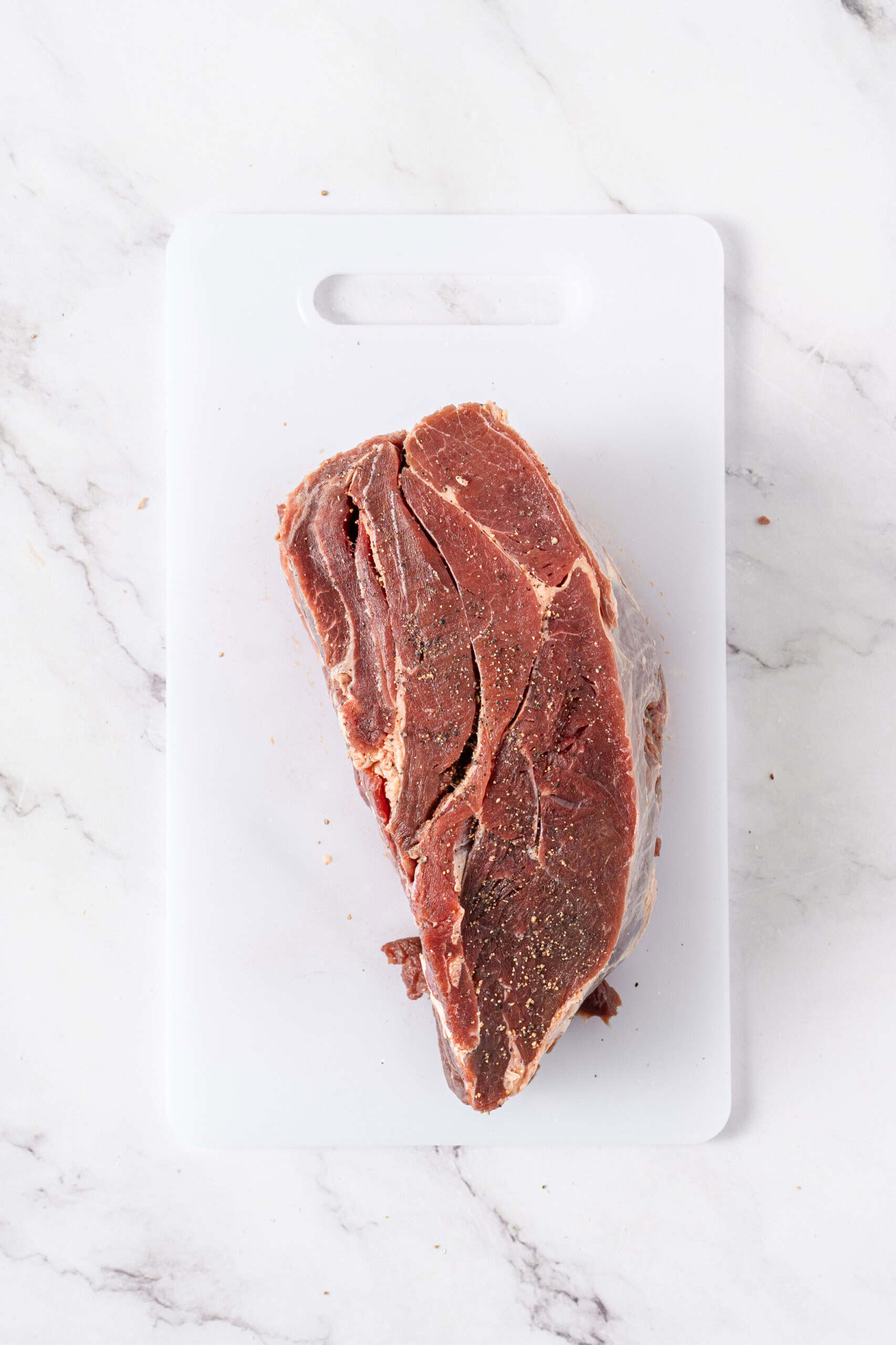 Raw beef roast seasoned with black pepper on a white cutting board.