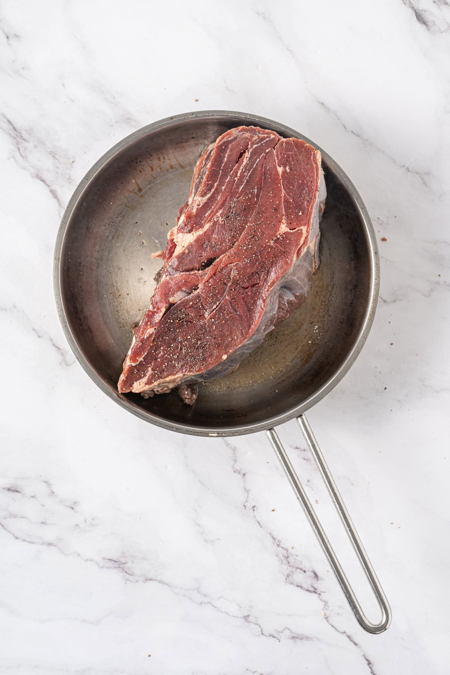 Seasoned beef roast placed in a hot skillet for searing.