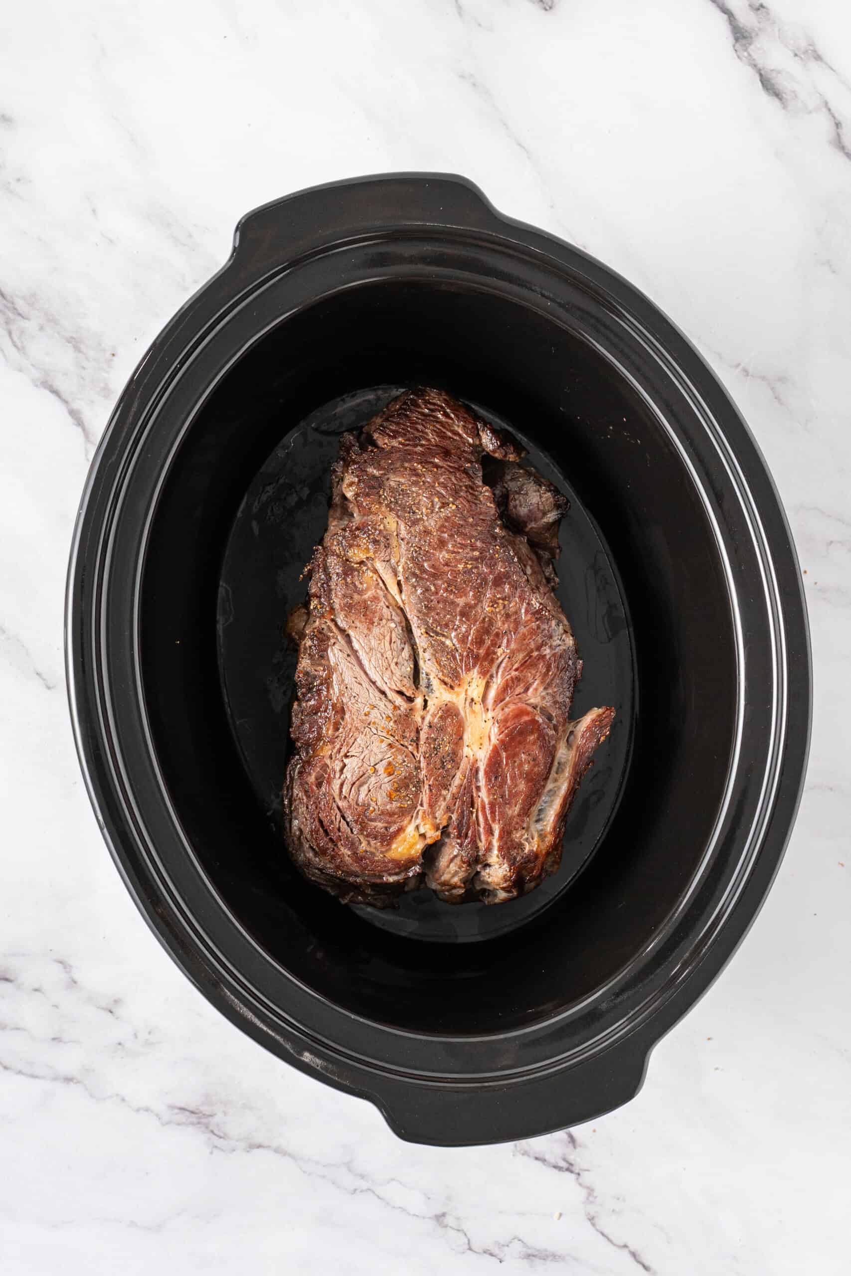 Seared beef roast placed in a slow cooker.