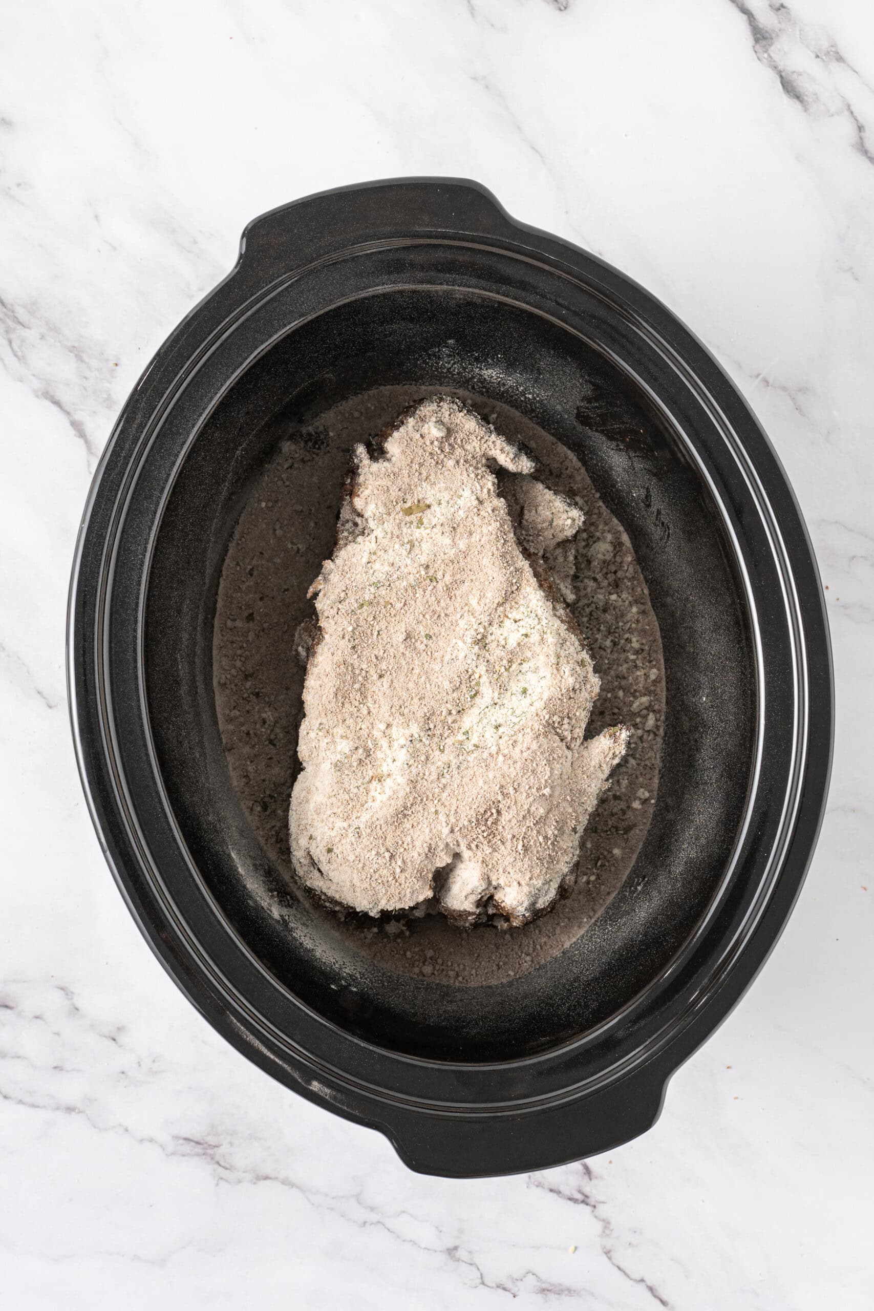 Seared beef roast covered with dry seasoning in a slow cooker.
