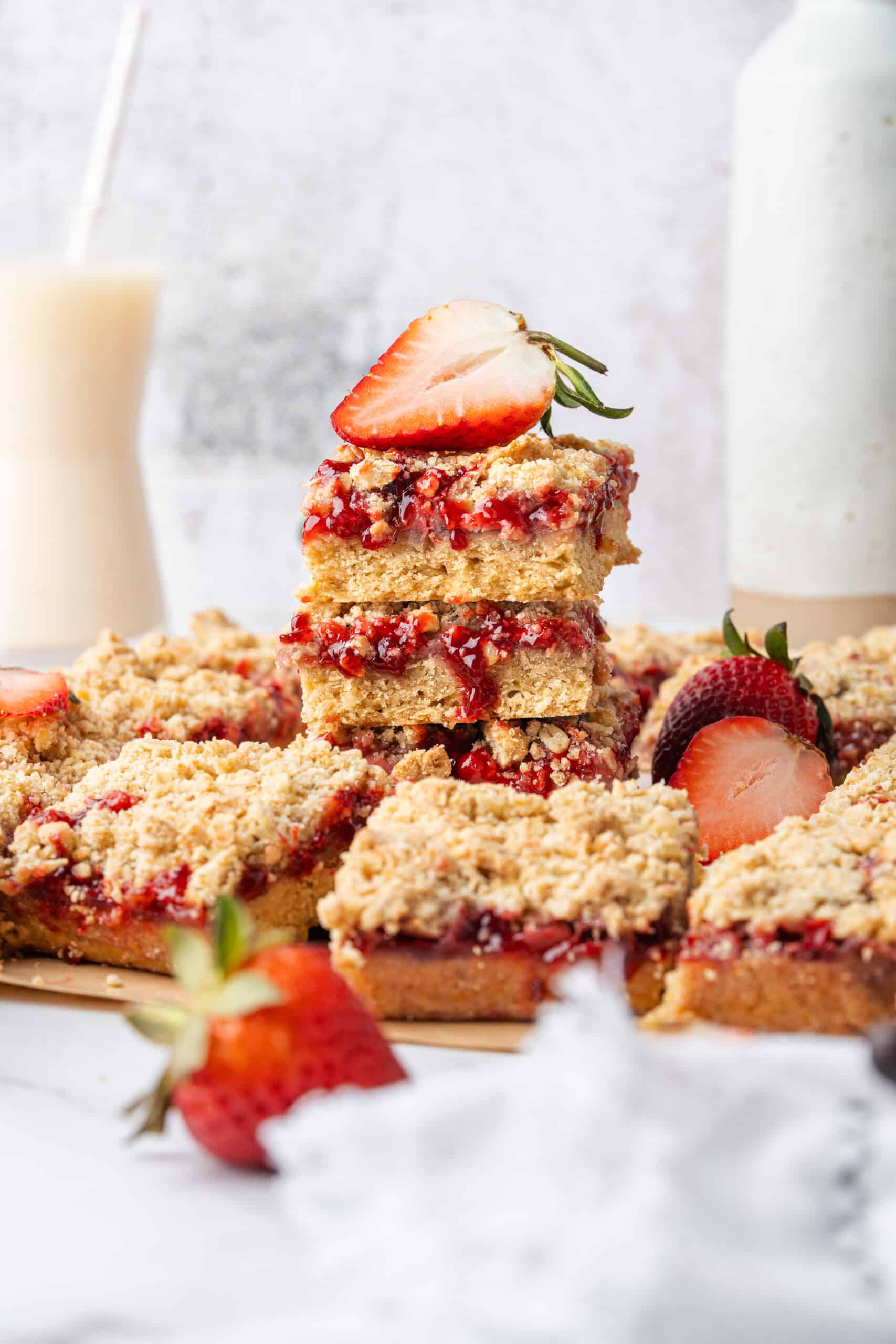 Stacked strawberry crumb bars surrounded by sliced bars and fresh strawberries.