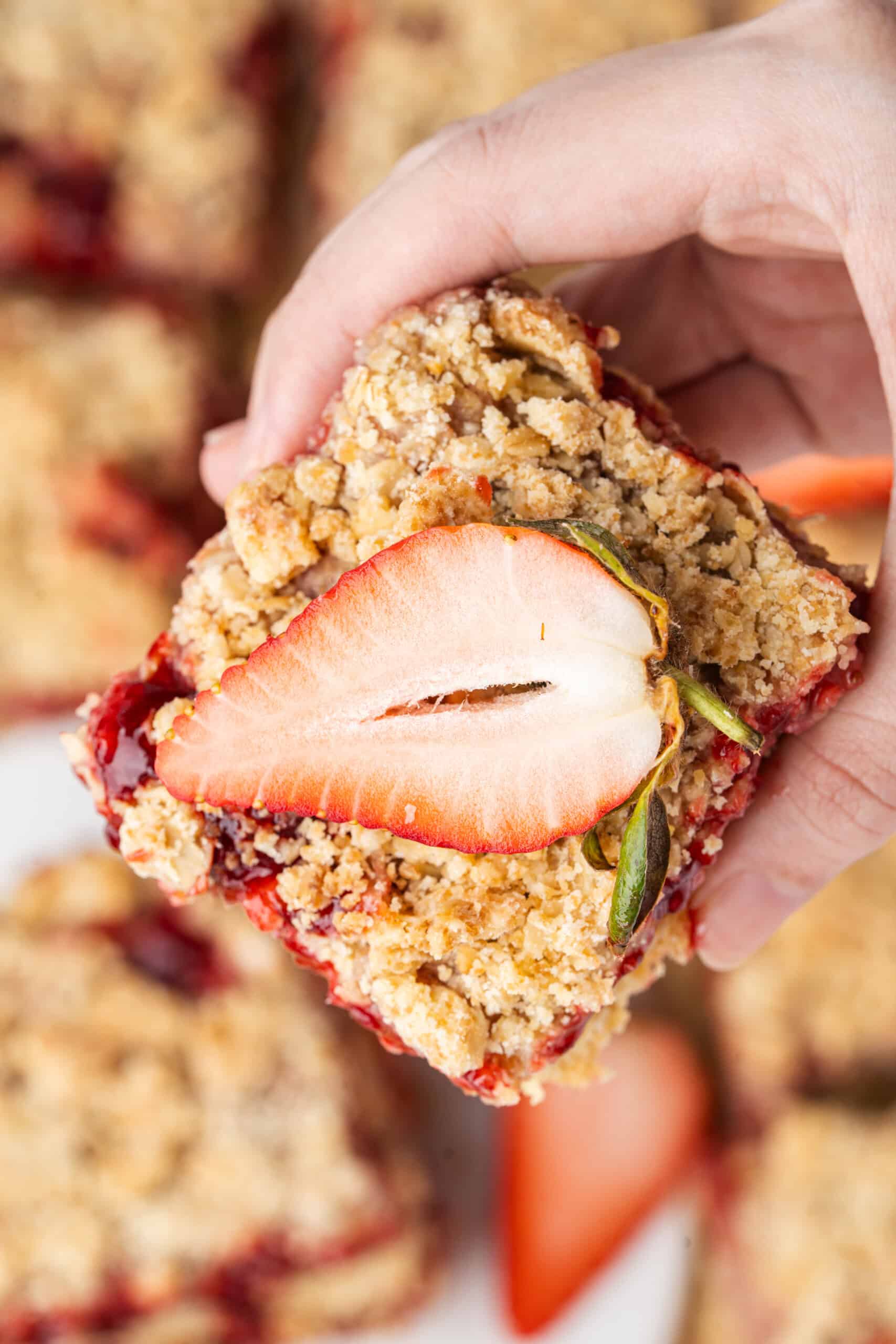 Strawberry crumb bar topped with a fresh strawberry half and held in one hand.