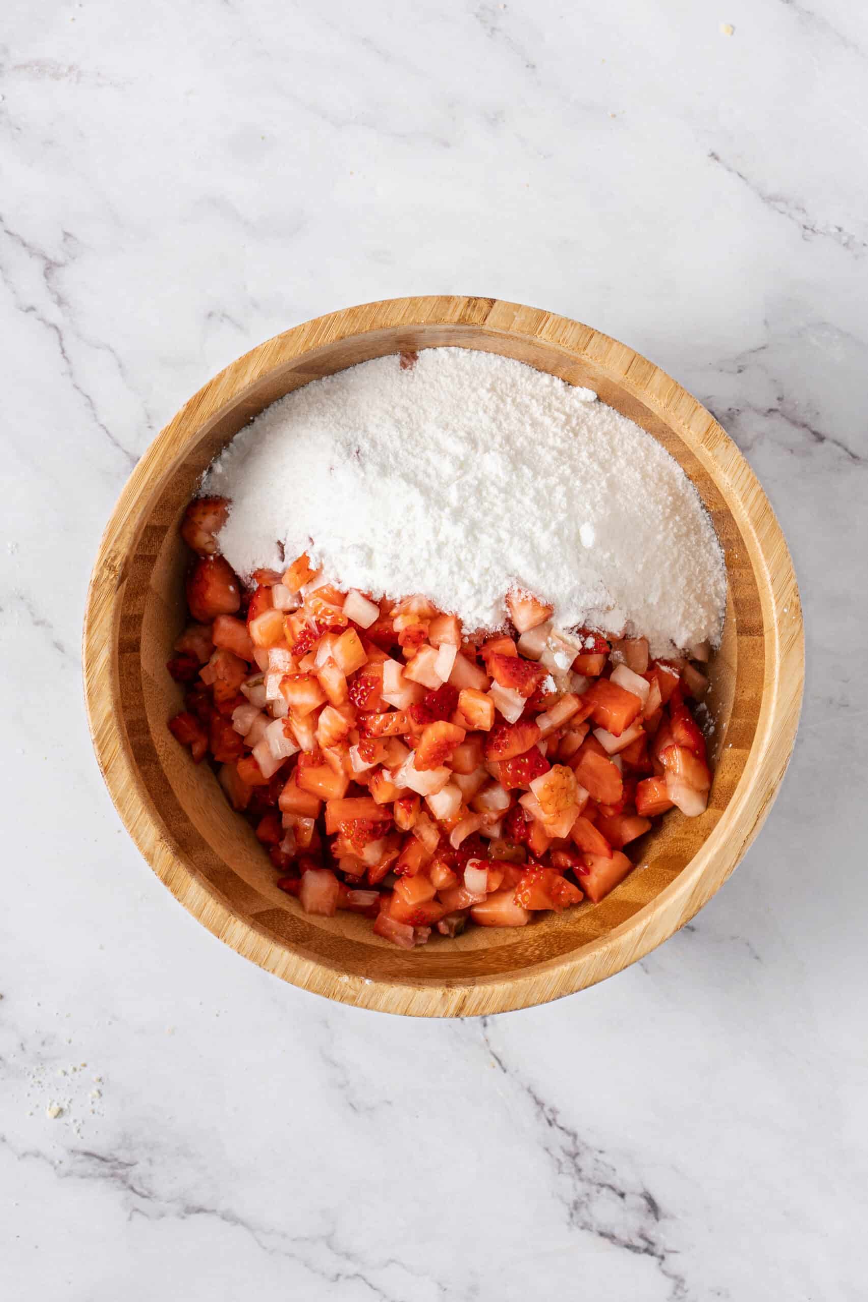 Chopped strawberries topped with the sugar and cornstarch mixture in a wooden bowl.