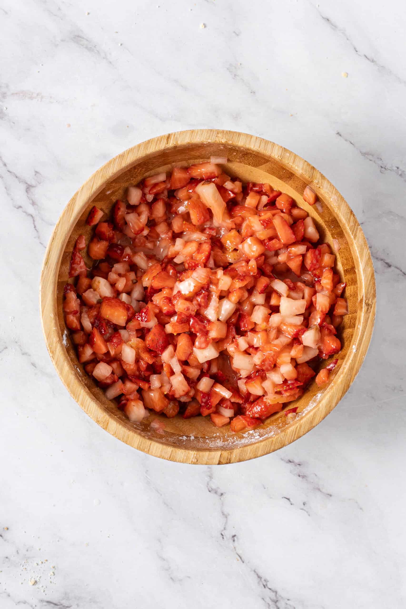 Chopped strawberries mixed with sugar and cornstarch in a wooden bowl.