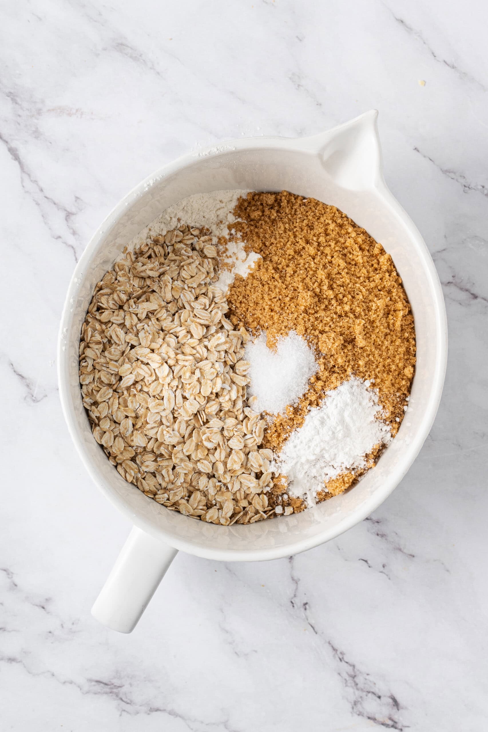 Rolled oats, brown sugar, flour, and other dry ingredients in a white mixing bowl.