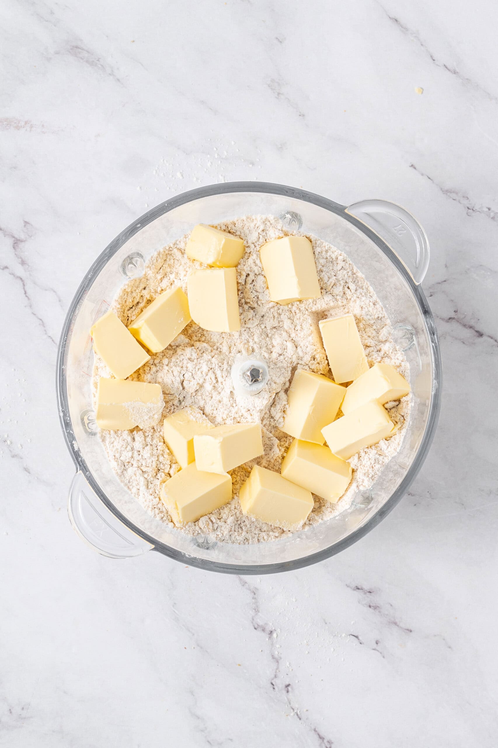 Cubed butter added to the dry oat mixture in a food processor.