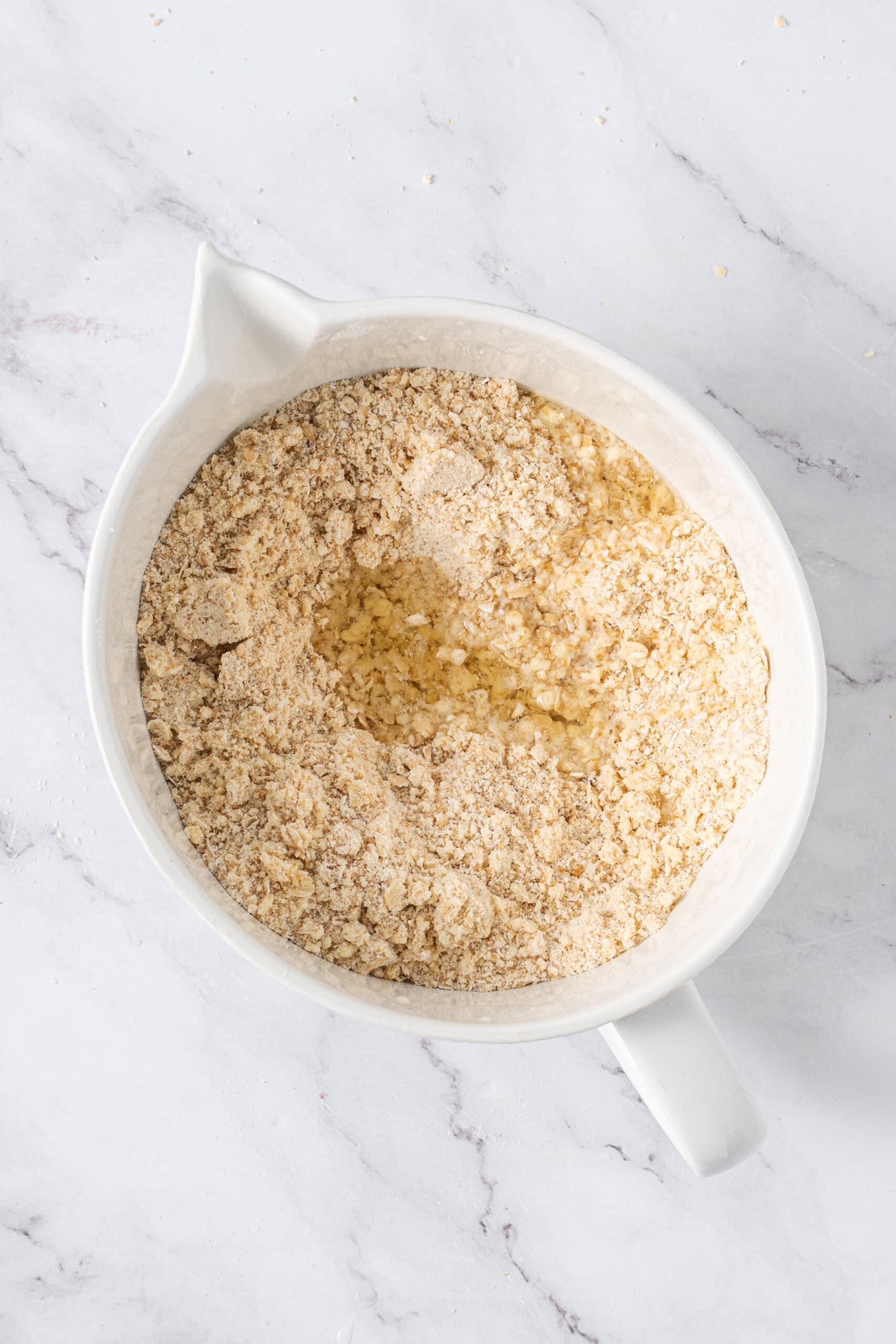Egg whites added to the crumb mixture in a white mixing bowl.
