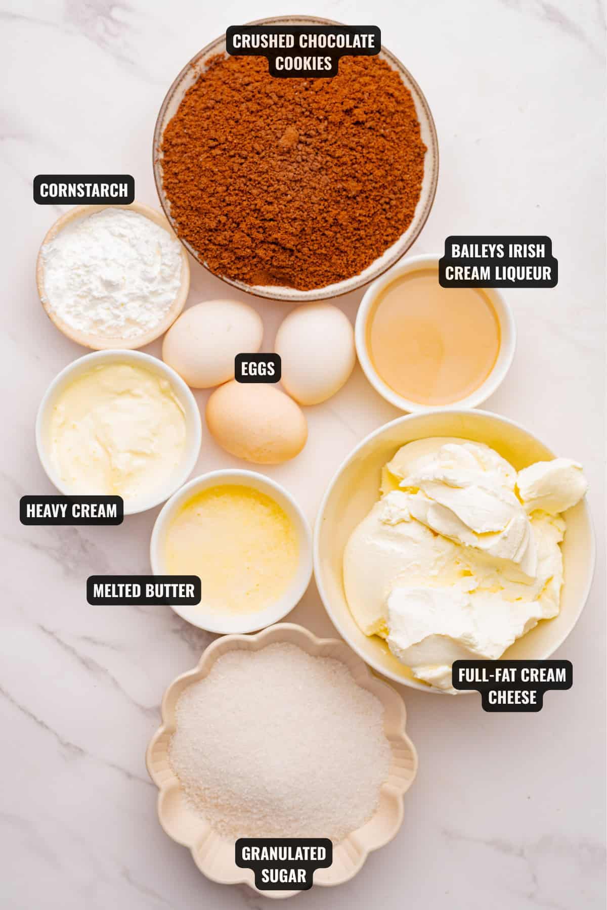ingredients for baileys irish cream cheesecake recipe including crushed chocolate cookies, cornstarch, eggs, irish cream liqueur, cream cheese, melted butter, heavy cream, and sugar.
