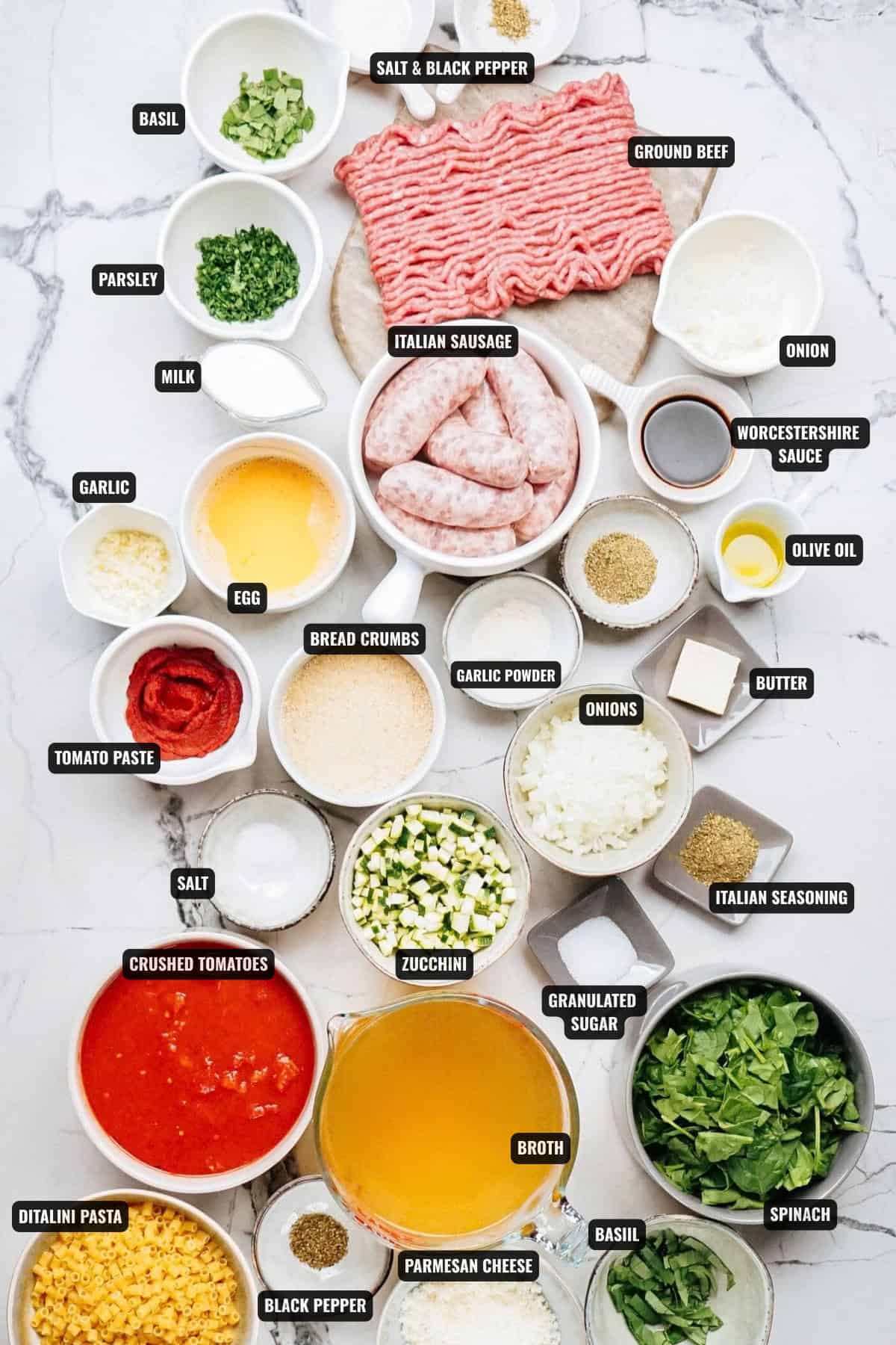 ingredients for italian meatball soup recipe including ground beef, italian sausage, onion, parsley, basil, milk, egg, garlic, worcestershire sauce, olive oil, butter, garlic powder, bread crumbs, tomato paste, crushed tomatoes, zucchini, granulated sugar, italian seasoning, spinach, parmesan cheese, broth, and ditalini pasta